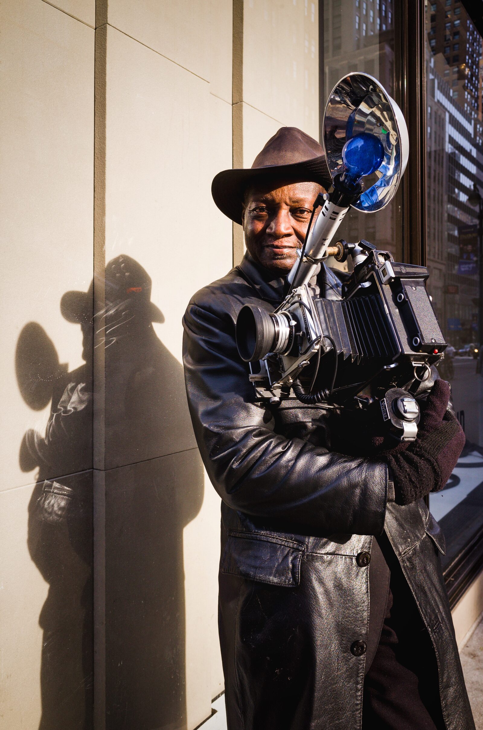Street photographer Louis Mendes holding a Graflex Speed Graphic camera with bulb flash on 5th Avenue, New York