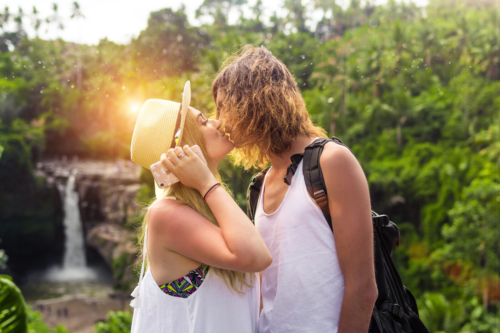 Newlywed couple sharing a kiss in front of a cascading waterfall, lush green foliage framing the romantic scene