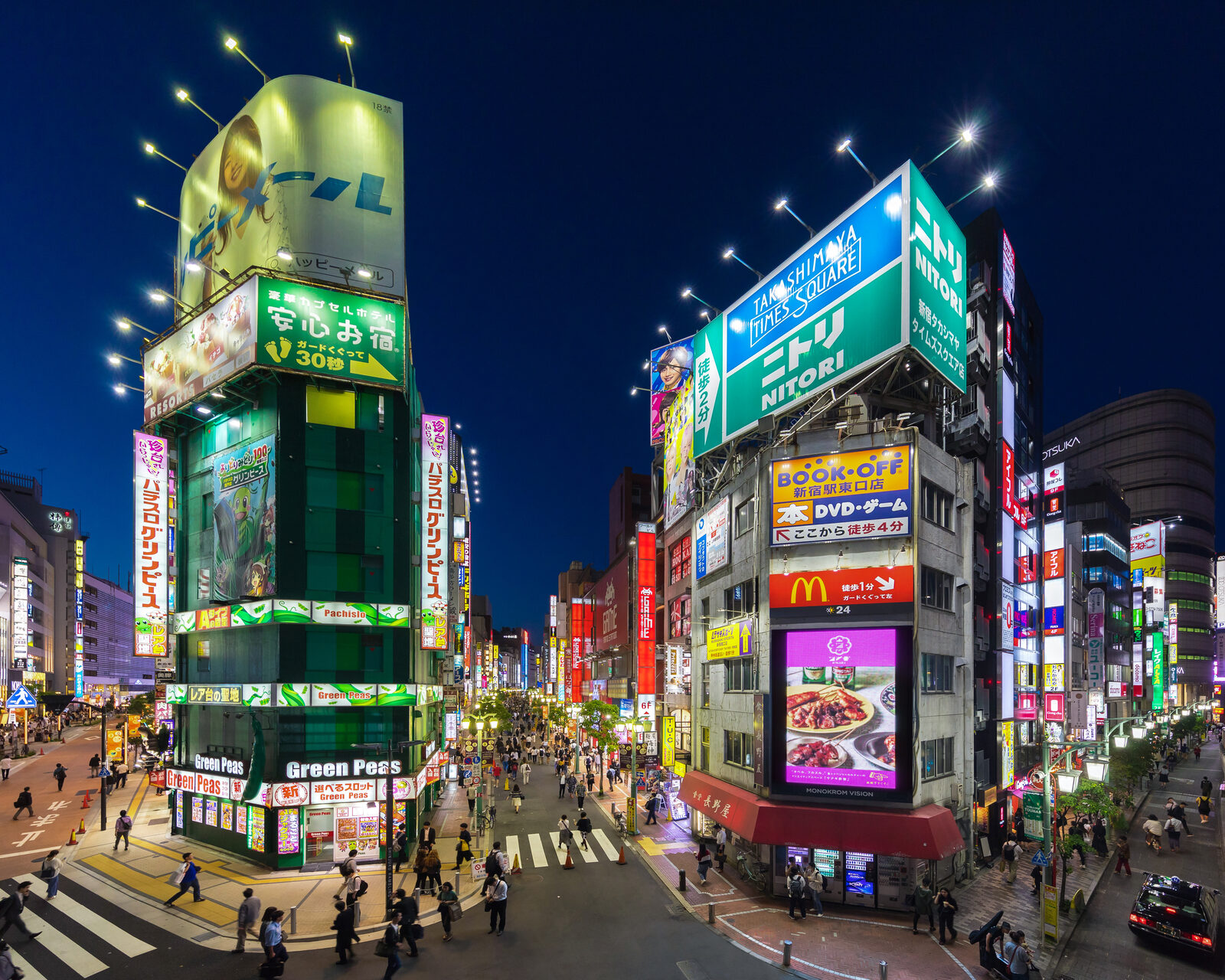Shinjuku street at blue hour lined with neon kanji signs in red, blue, and white, pedestrians silhouetted on the wet pavement