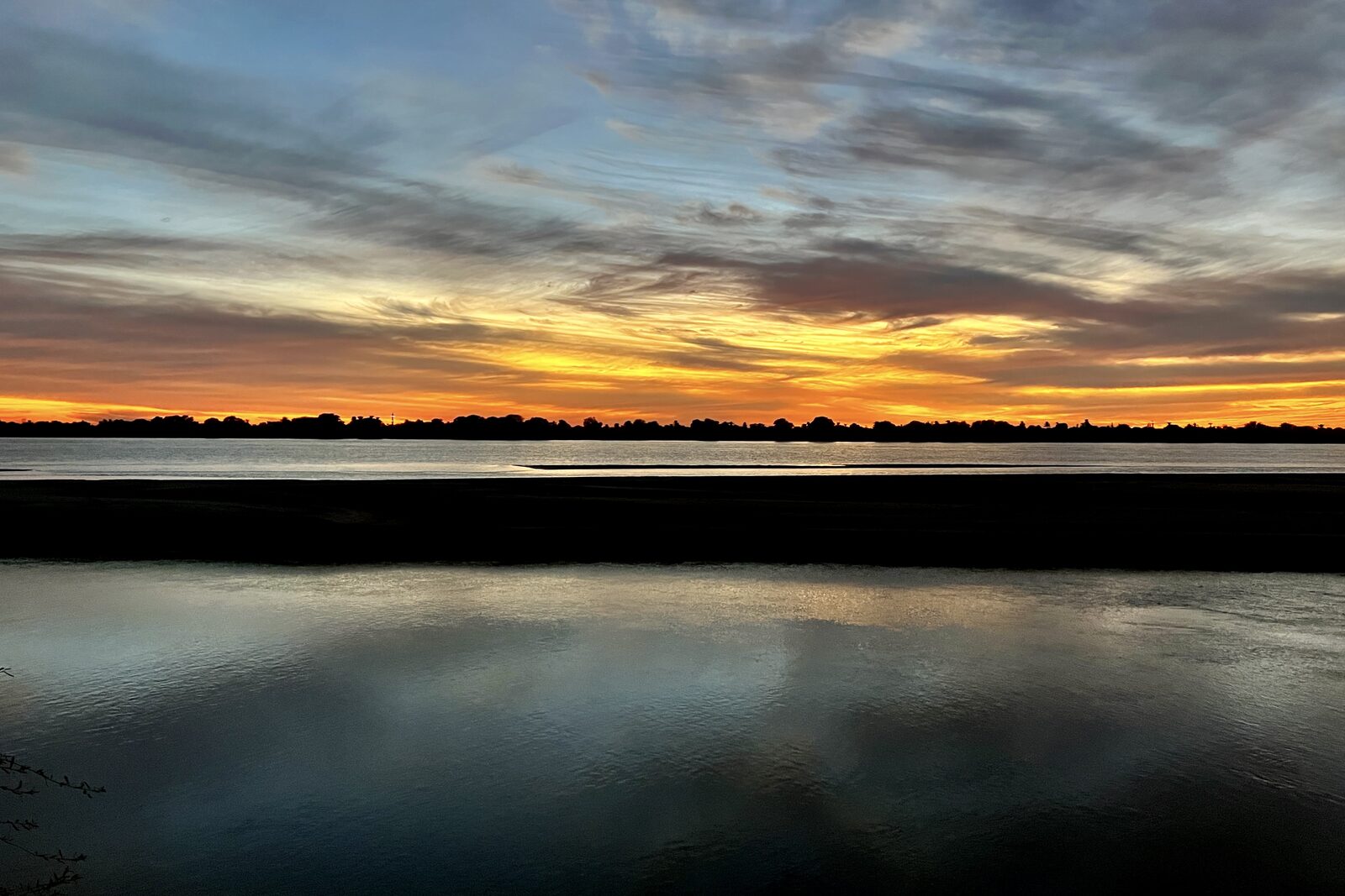 Magnificent dusk sky with vivid orange and purple clouds reflected over still water and silhouetted shoreline