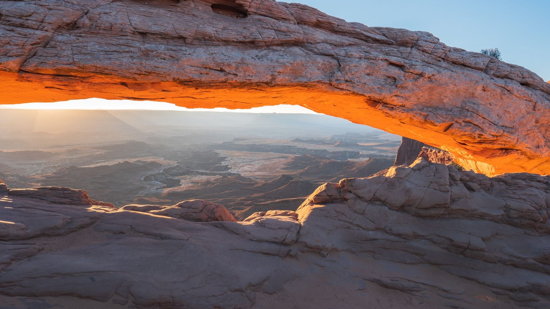 Warm orange light along the underside of Mesa Arch above a shaded rocky foreground