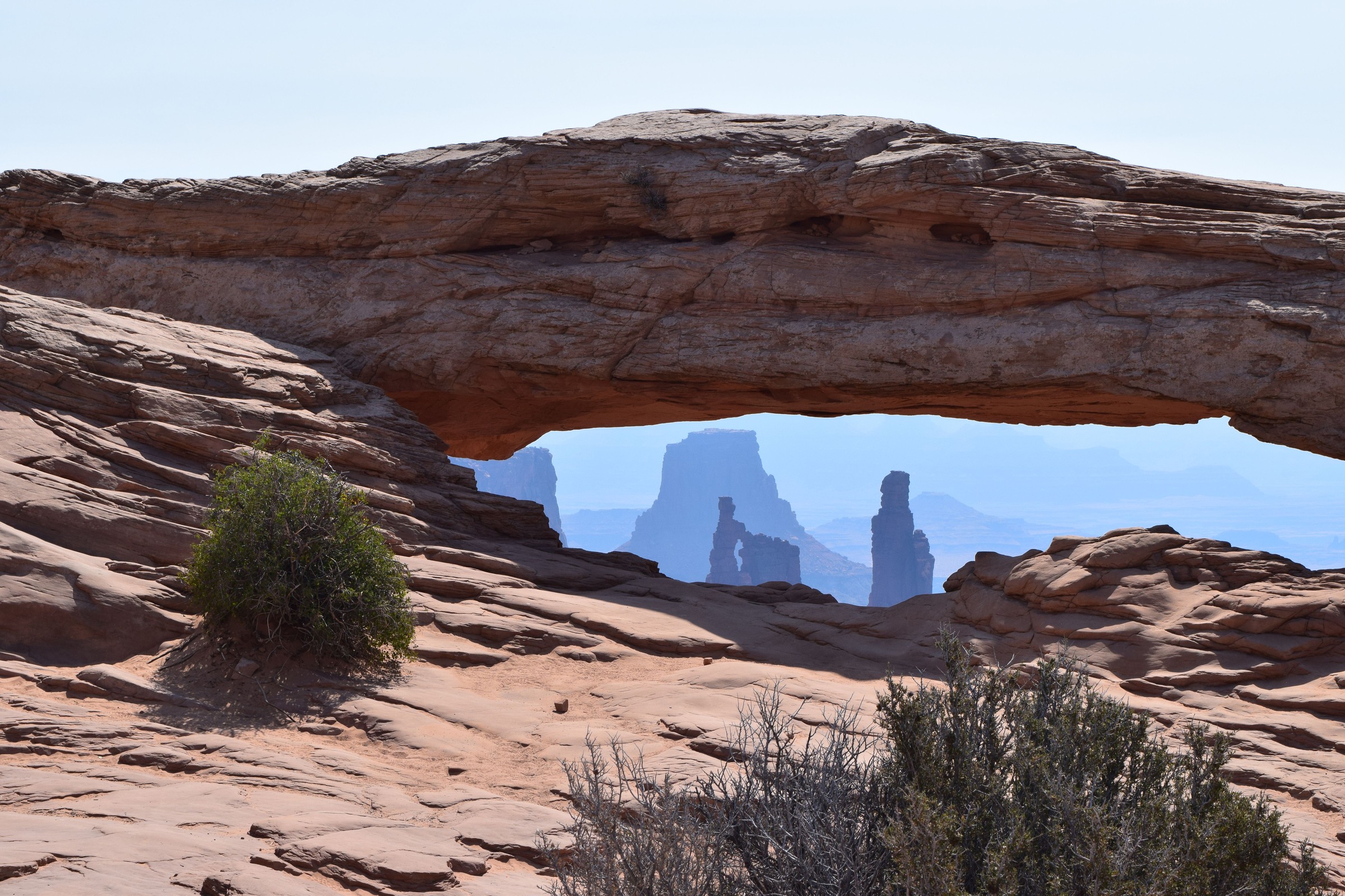 Mesa Arch framing distant towers above sandstone and desert plants