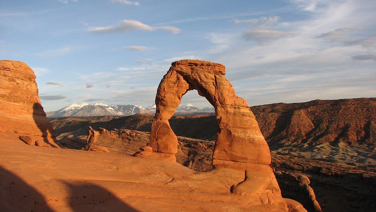 Sandstone Delicate Arch glowing red at sunset with La Sal Mountains demonstrating a travel photography composition.