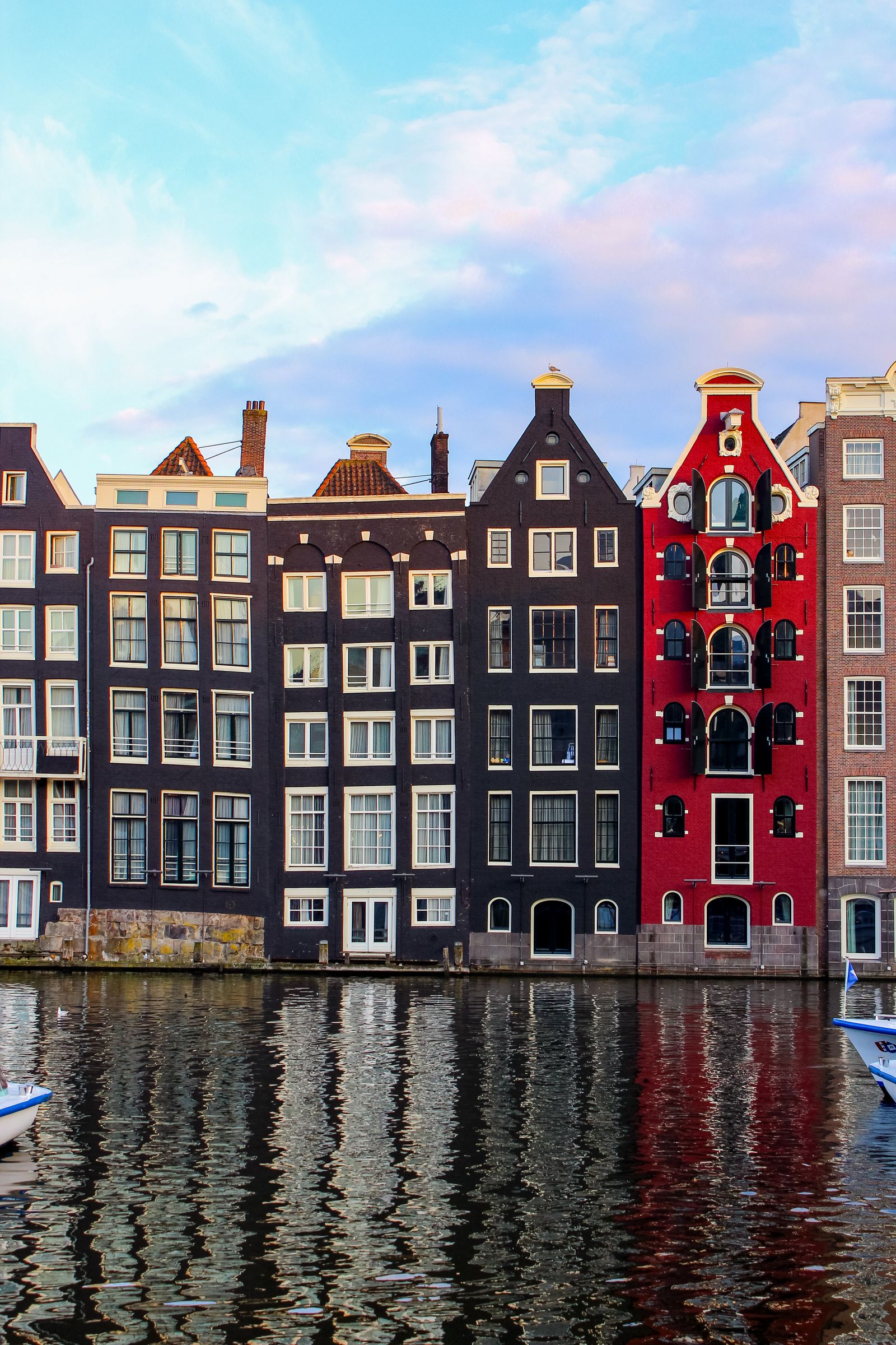 Colorful gabled Amsterdam canal houses reflected in still water beneath a pastel sky