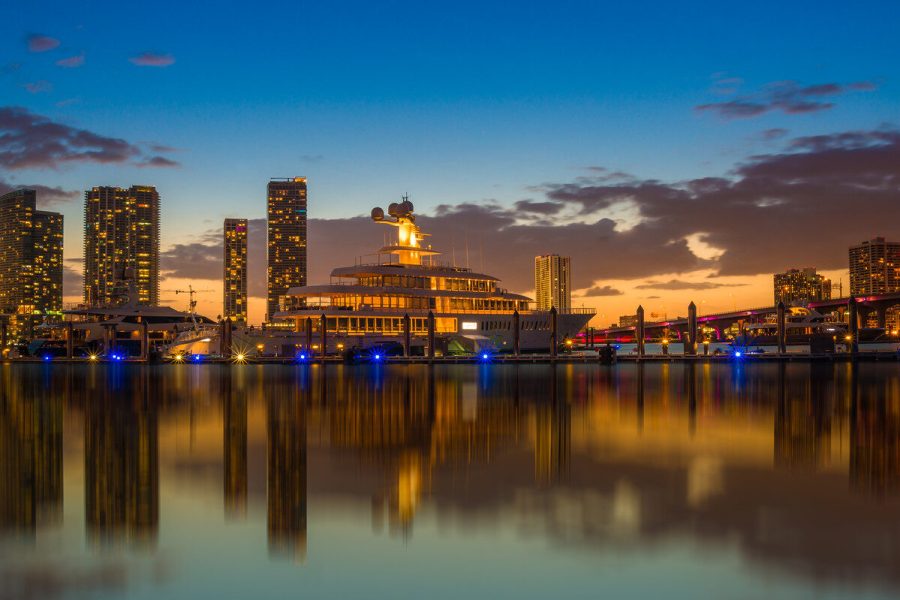 Miami skyline and illuminated yacht reflected in calm water at blue hour, photographed by Edin Chavez
