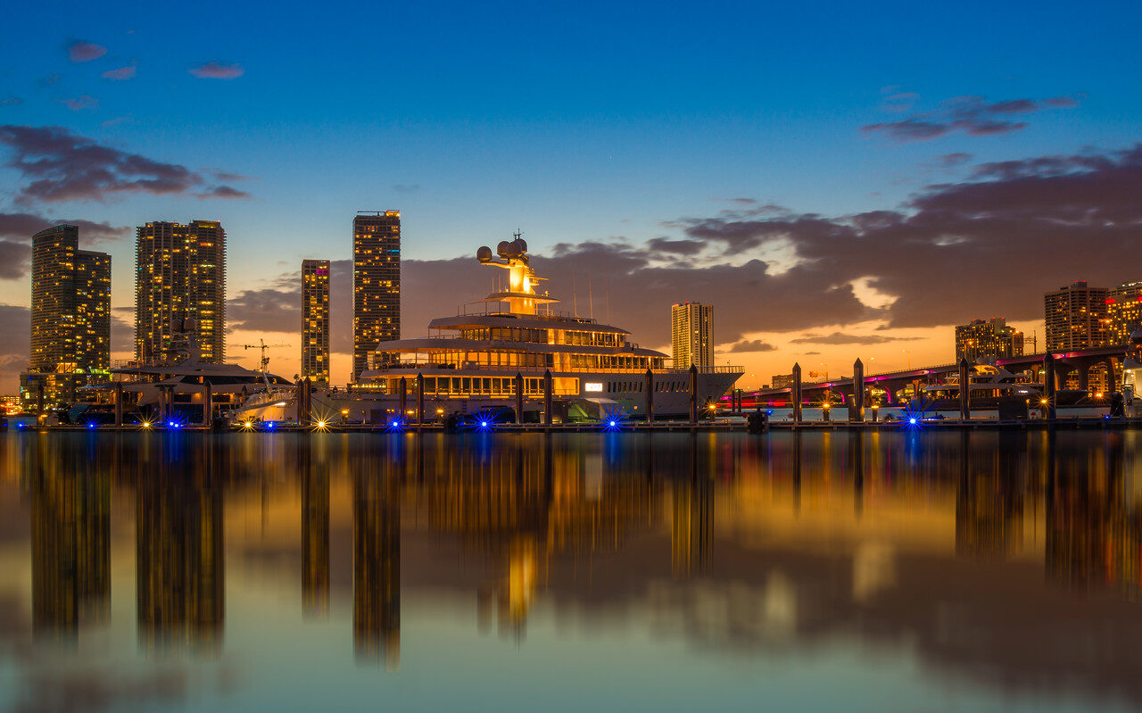 Miami skyline and illuminated yacht reflected in calm water at blue hour, photographed by Edin Chavez