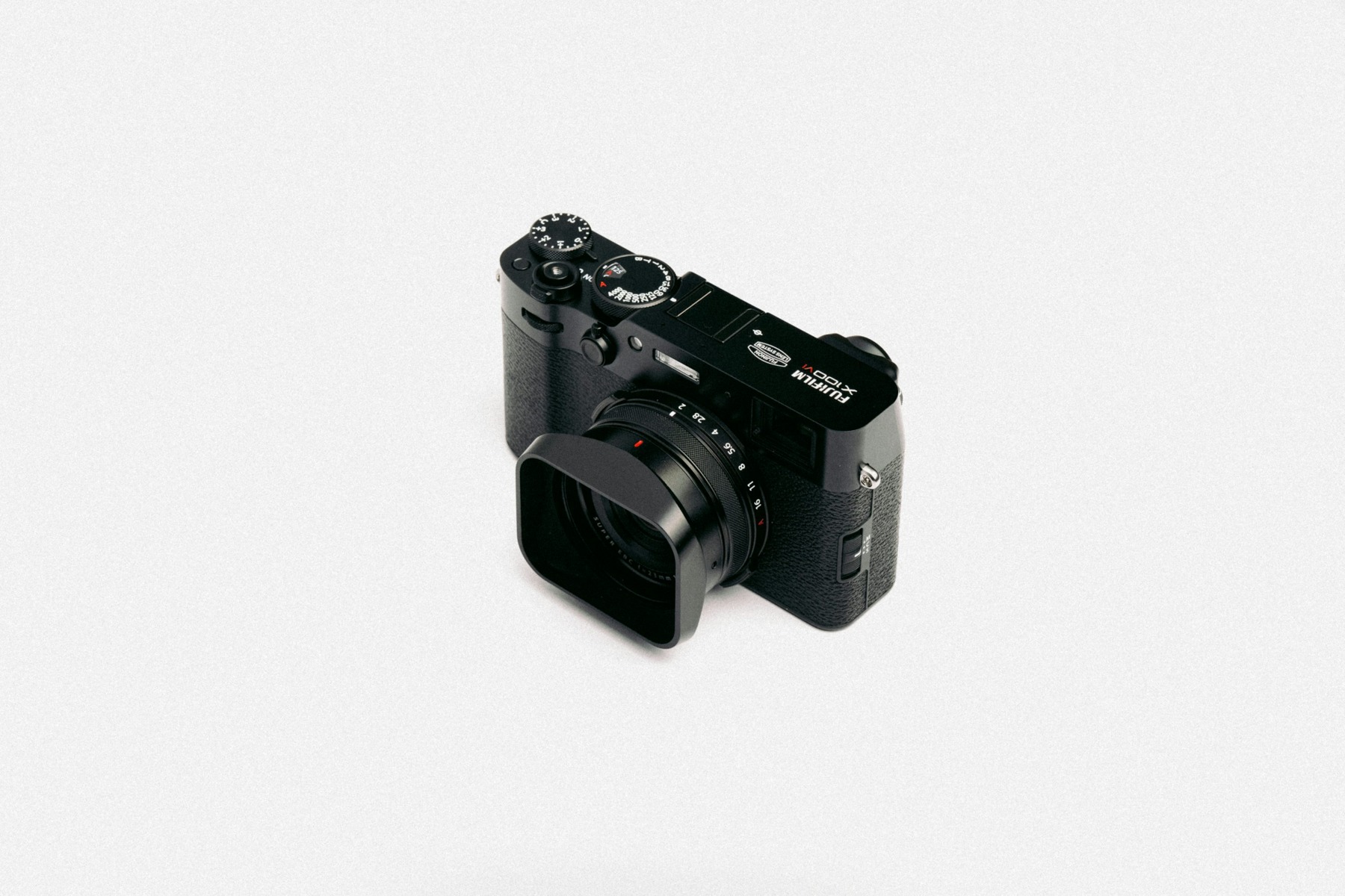Black Fujifilm X100VI fixed-lens camera with lens hood photographed on a light studio surface