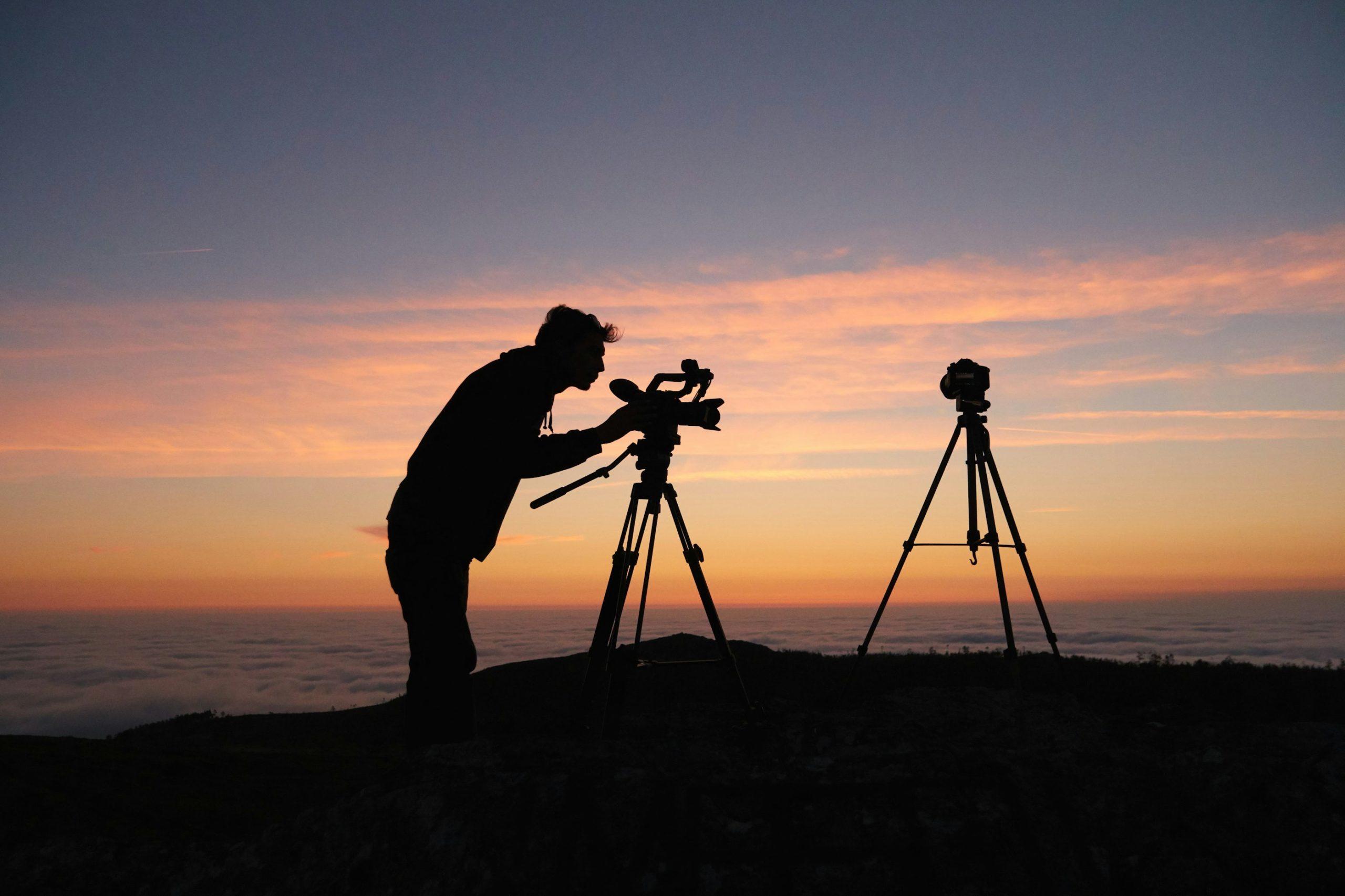 Photographer silhouetted against a sunset while using cameras on tripods in the mountains of Monchique, Portugal