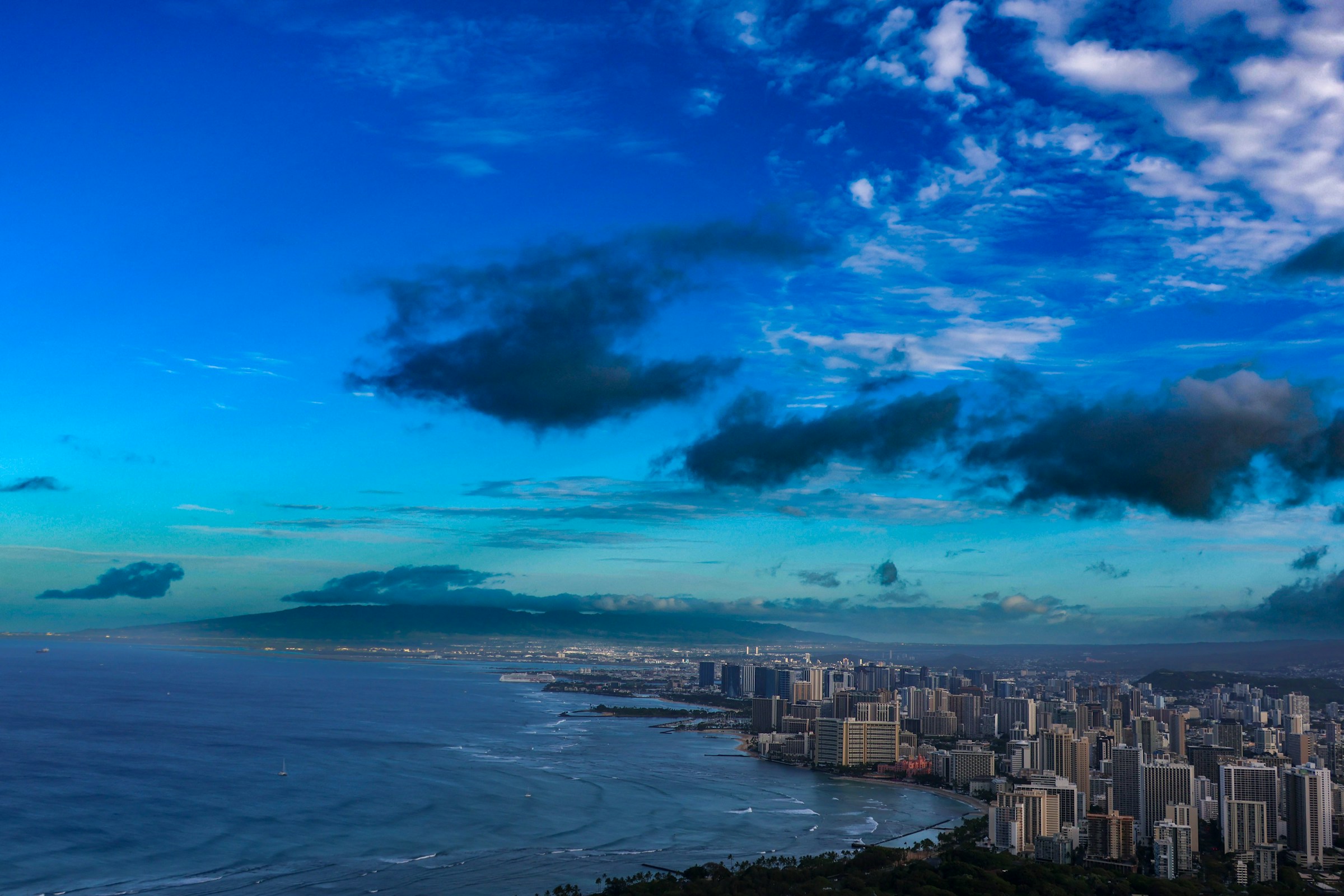 Waikiki shoreline and Honolulu skyline seen from Diamond Head beneath deep blue evening clouds