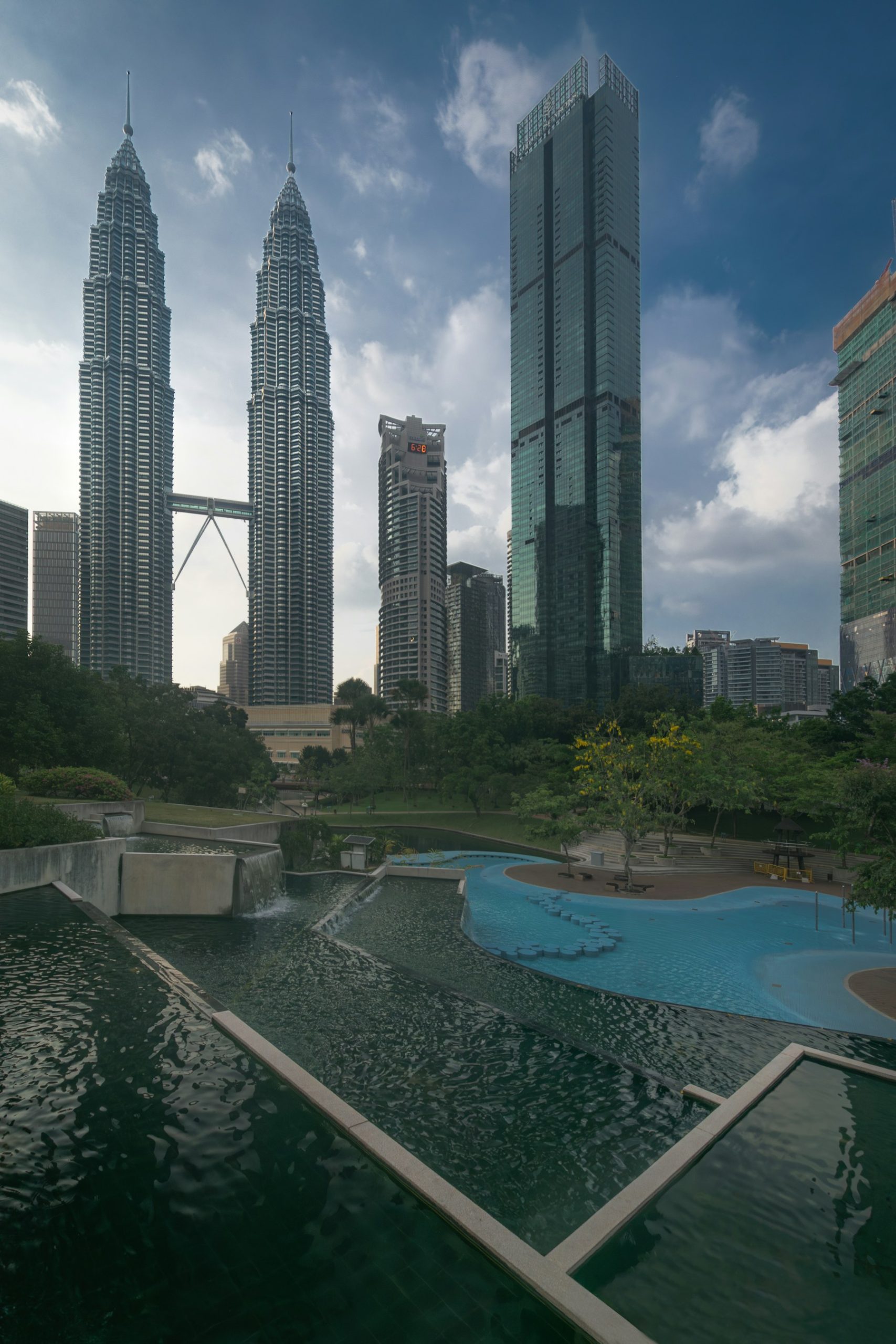 Two Petronas towers beyond the KLCC Park pool and fountains at dusk.