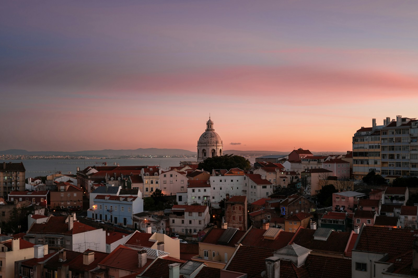Lisbon rooftops and the National Pantheon dome beneath a pink sunset sky