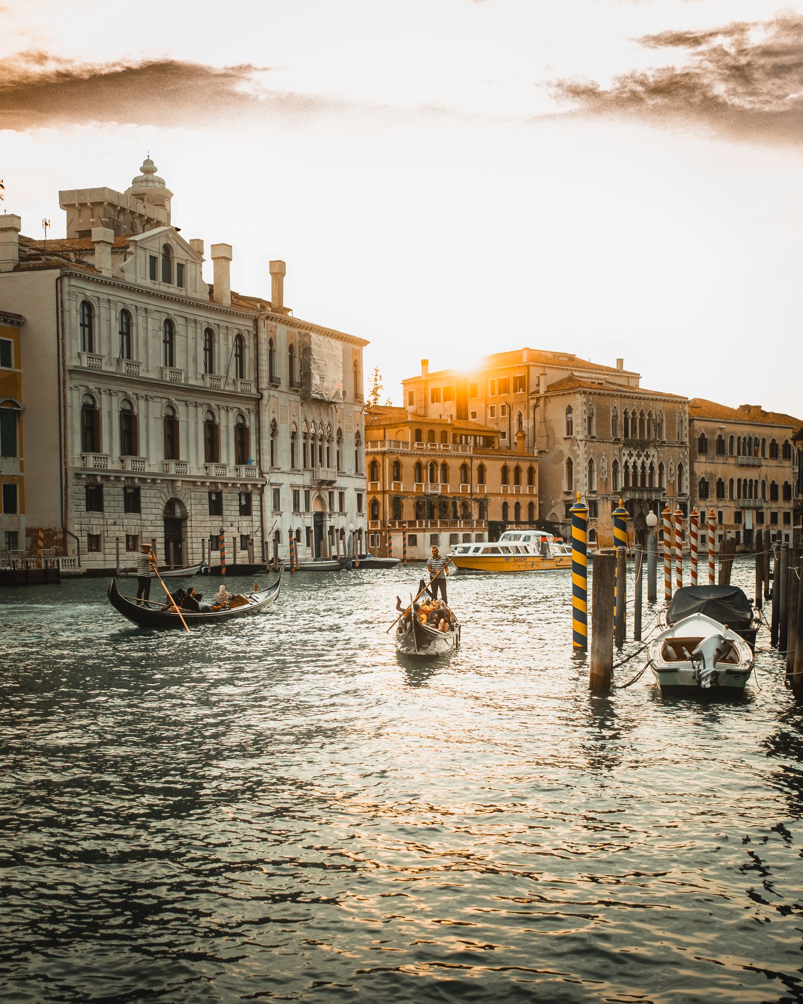 Gondolas moving along a Venice canal between sunlit historic buildings at sunset
