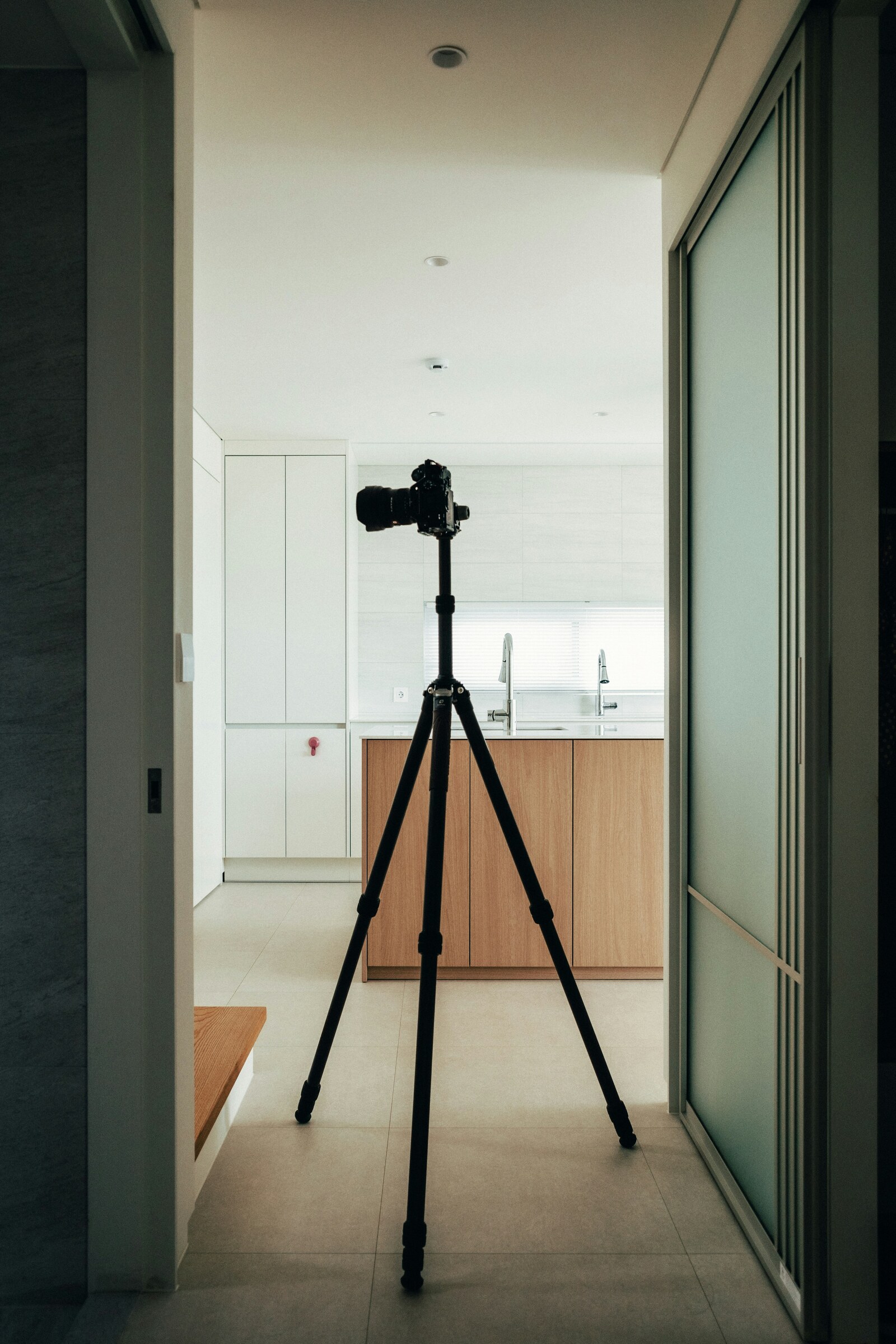 Camera mounted on a tall tripod in a hallway facing a bright kitchen
