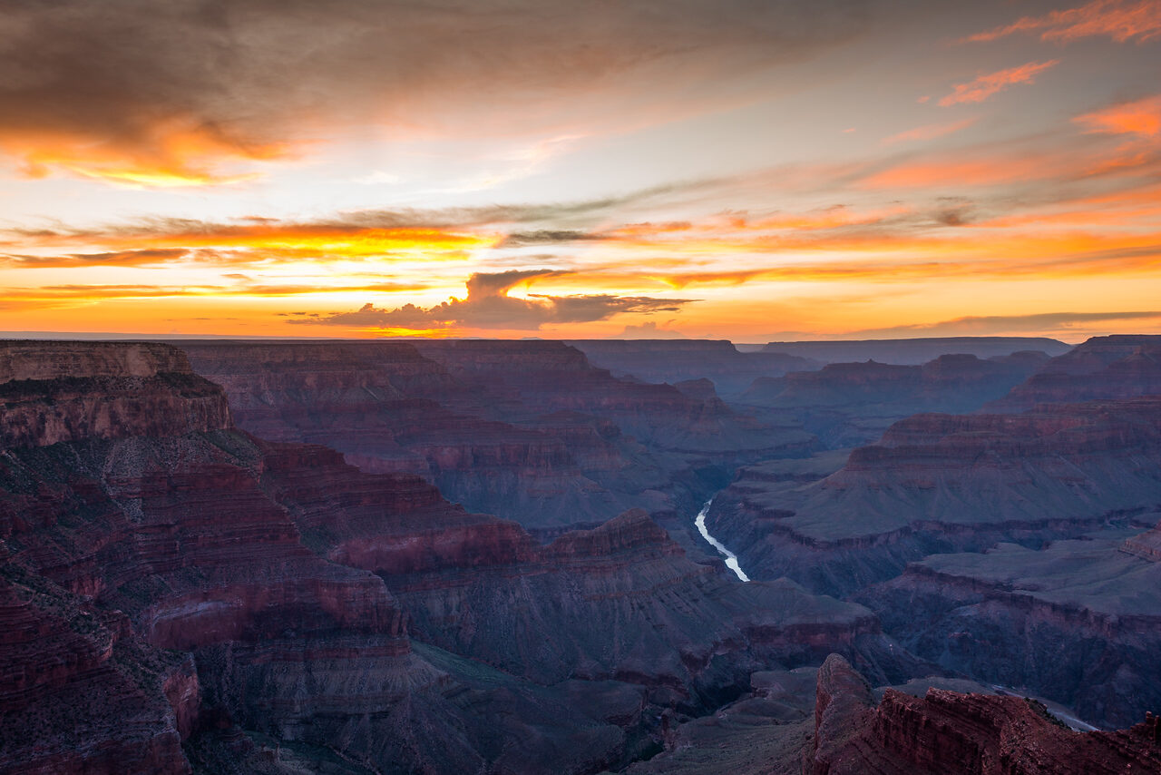 Colorado River winding through the Grand Canyon beneath orange sunset clouds