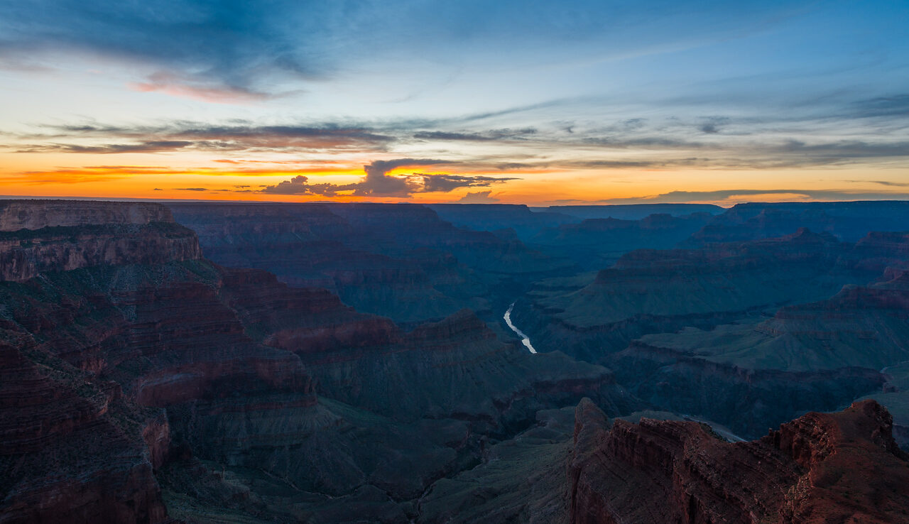 Grand Canyon ridges and the Colorado River beneath a warm sunset sky