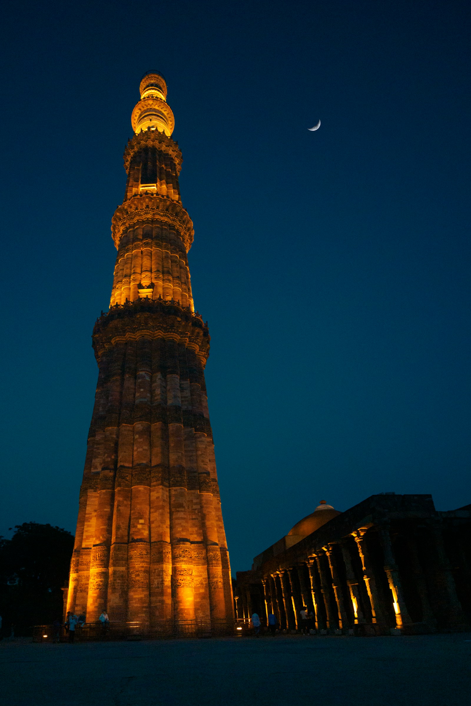 Illuminated Qutub Minar beneath a crescent moon at blue hour
