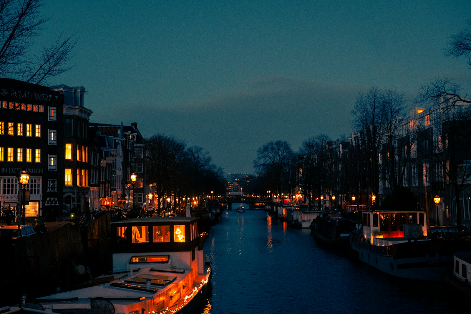 Houseboats and glowing windows along an Amsterdam canal in deep blue twilight