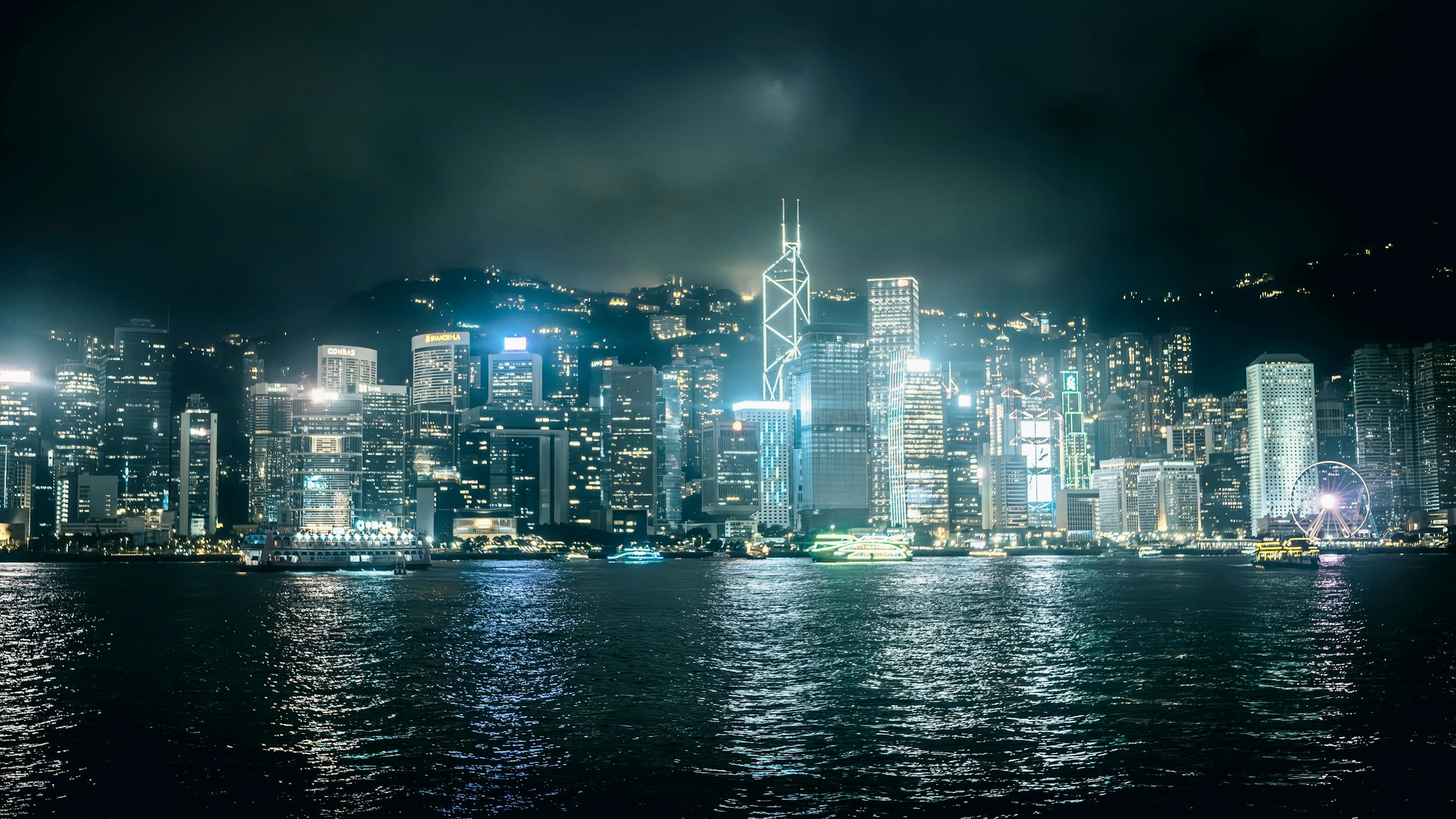 Hong Kong Island skyline panorama at night across Victoria Harbour with the Observation Wheel lit up
