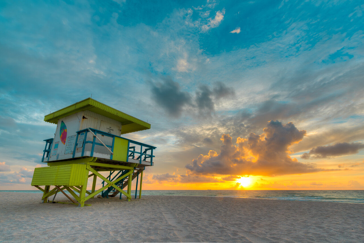 Green and white lifeguard tower on Miami Beach beside the ocean as the sun rises beneath dramatic clouds