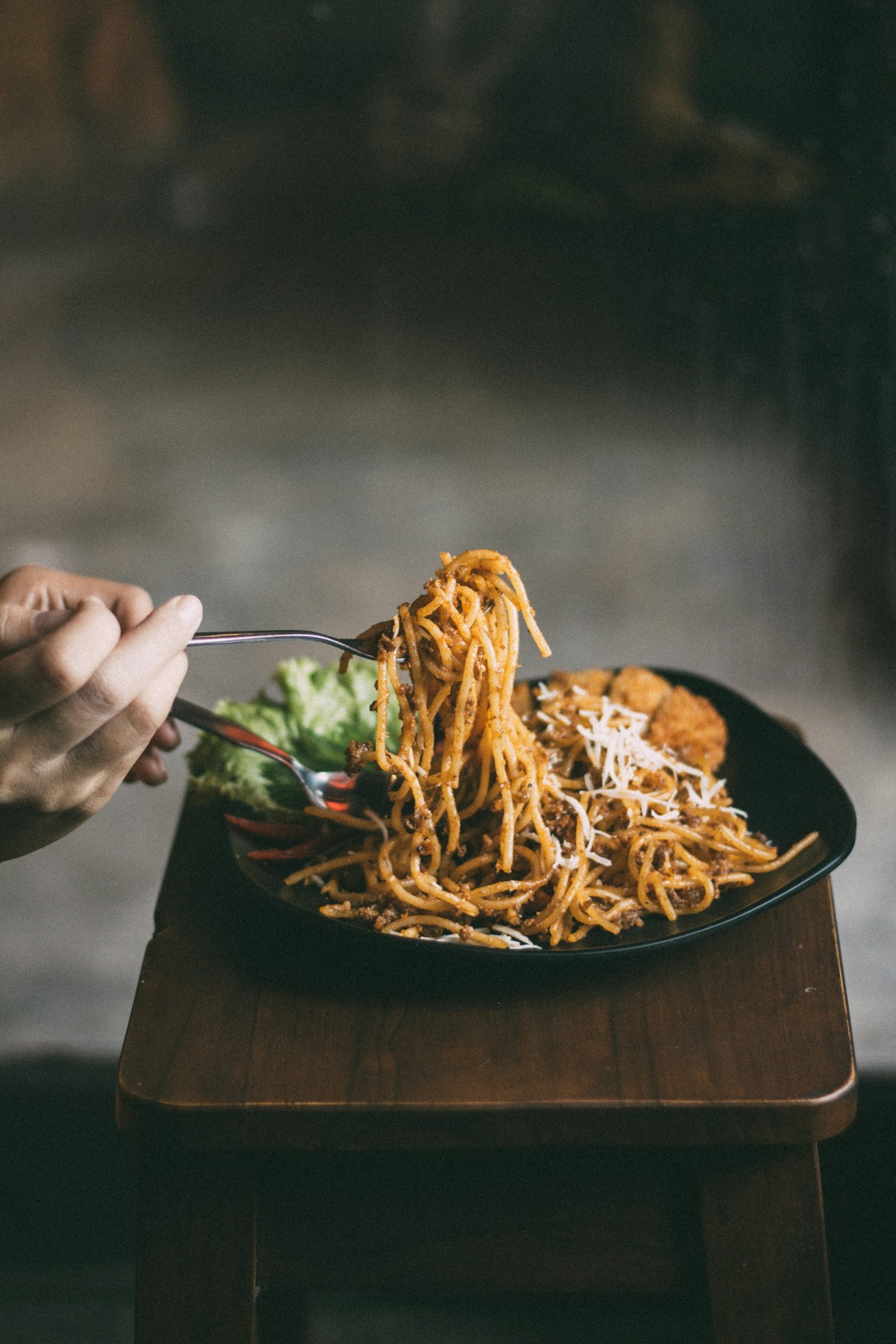 Pasta lifted with a fork above a black plate in a low-angle food photograph