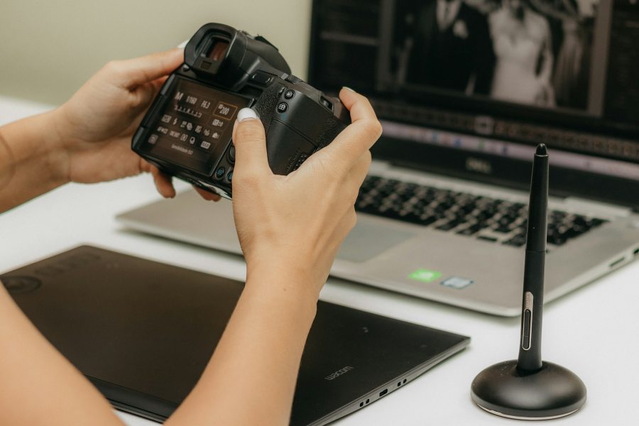 Photographer holding a camera in front of a laptop and drawing tablet.
