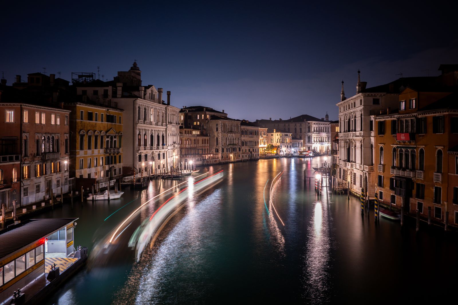 Boat light trails curve along Venice's Grand Canal between illuminated palazzi at night