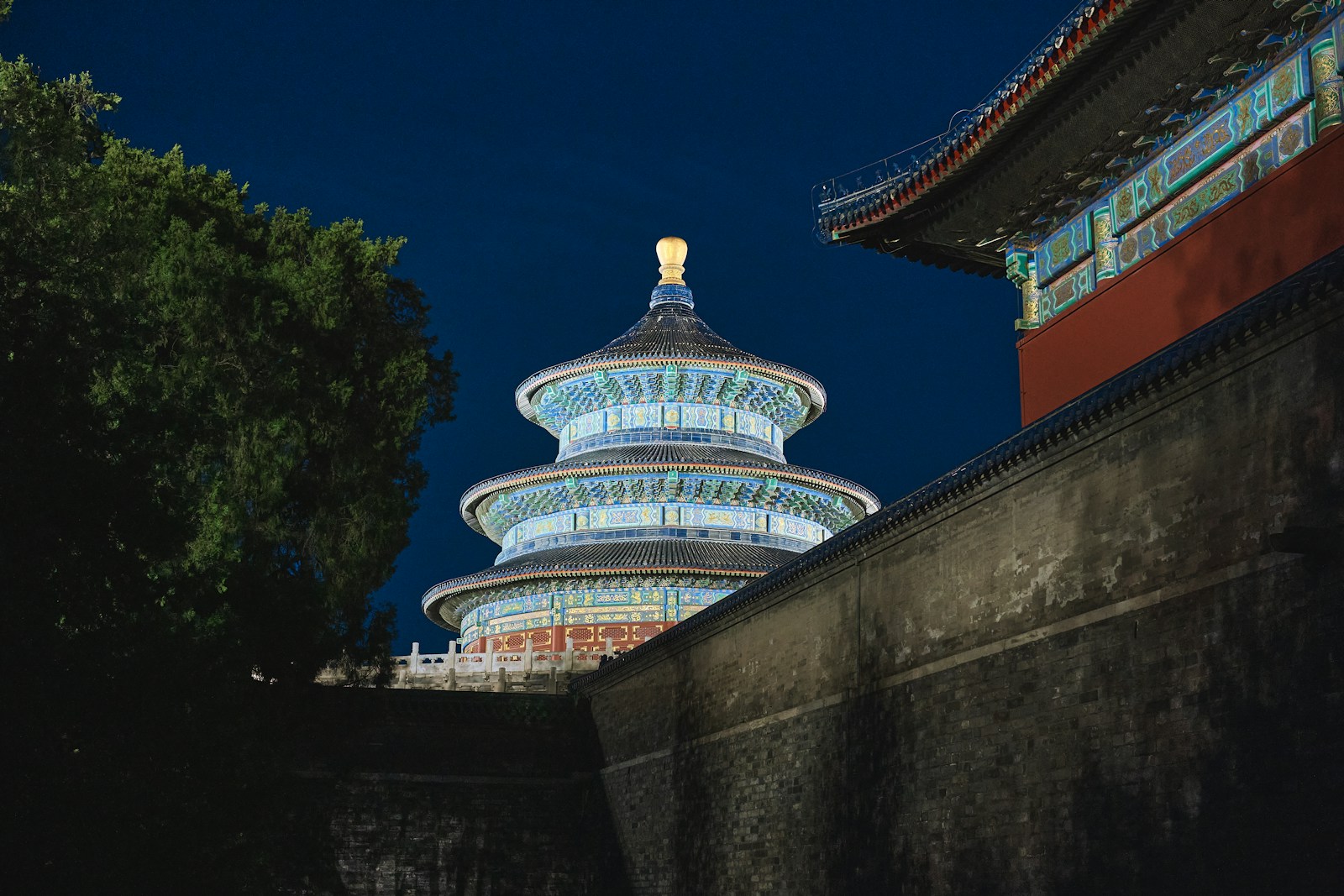 Illuminated Hall of Prayer for Good Harvests at night behind a courtyard wall