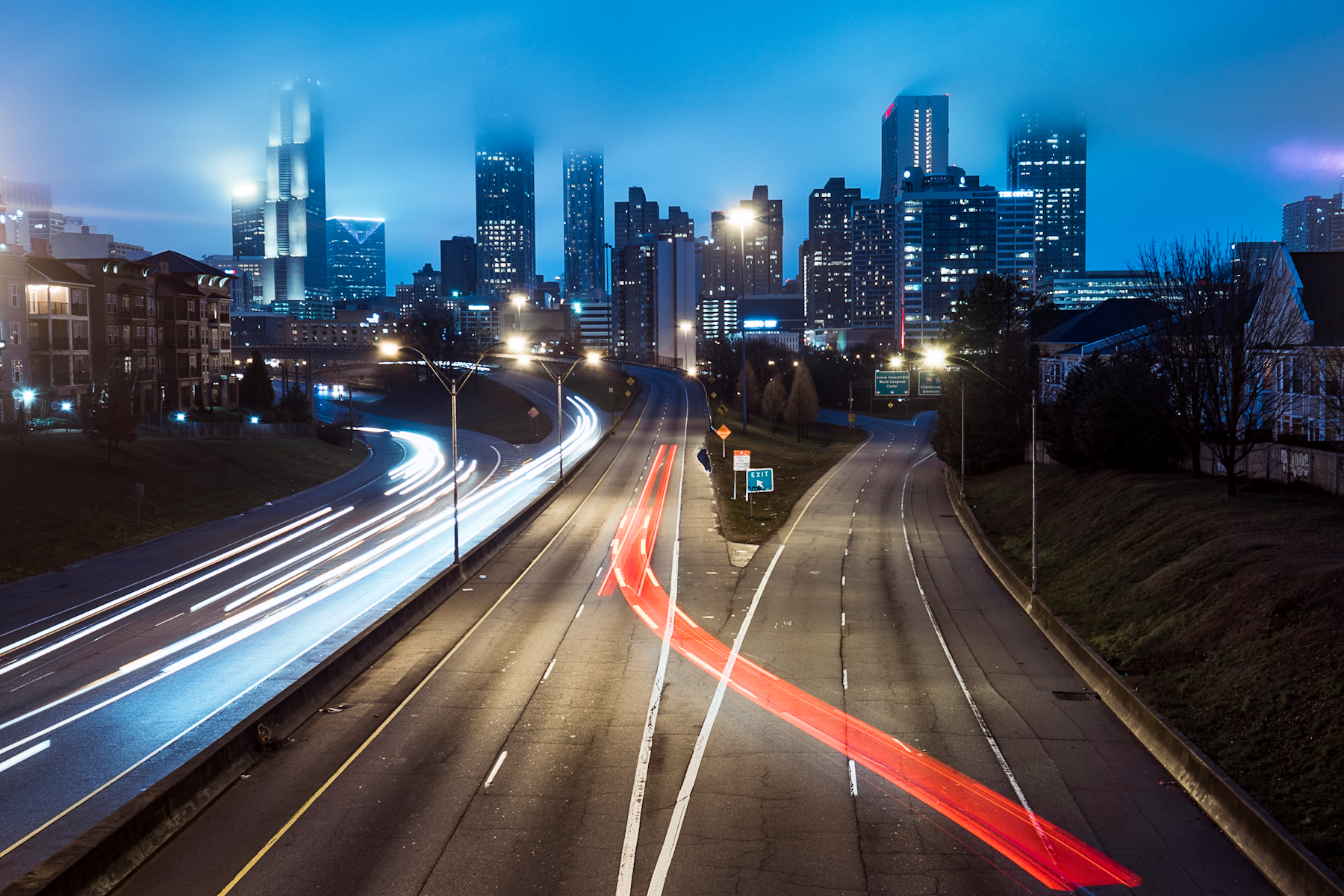Traffic light trails on a multi-lane highway at night with a city skyline beyond