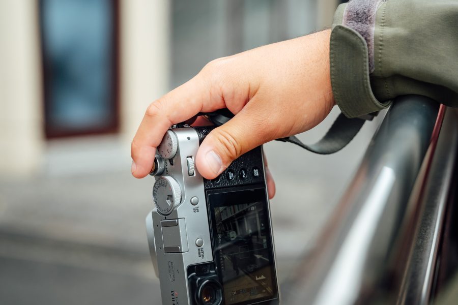 A hand holding a Fujifilm camera on a city street.