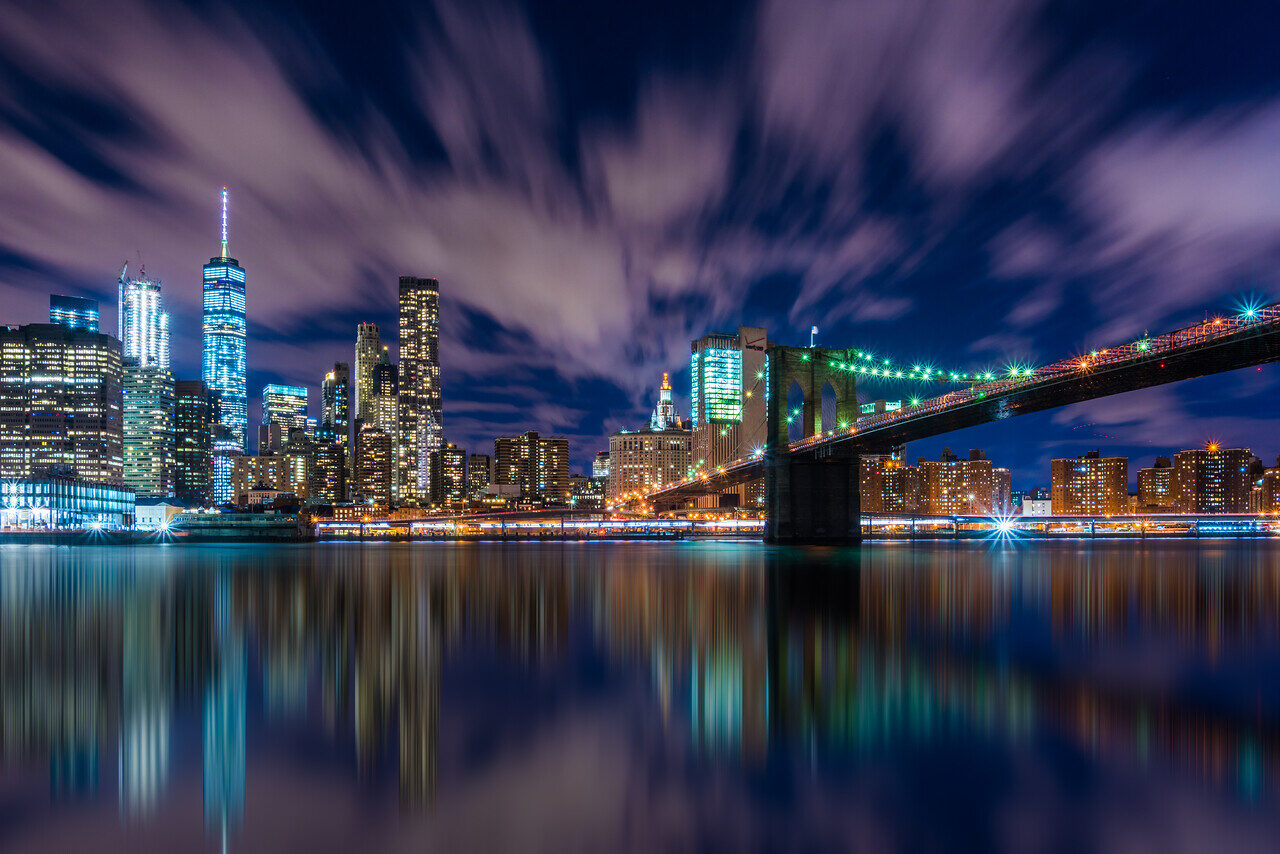 Brooklyn Bridge and Lower Manhattan skyline at night with river reflections