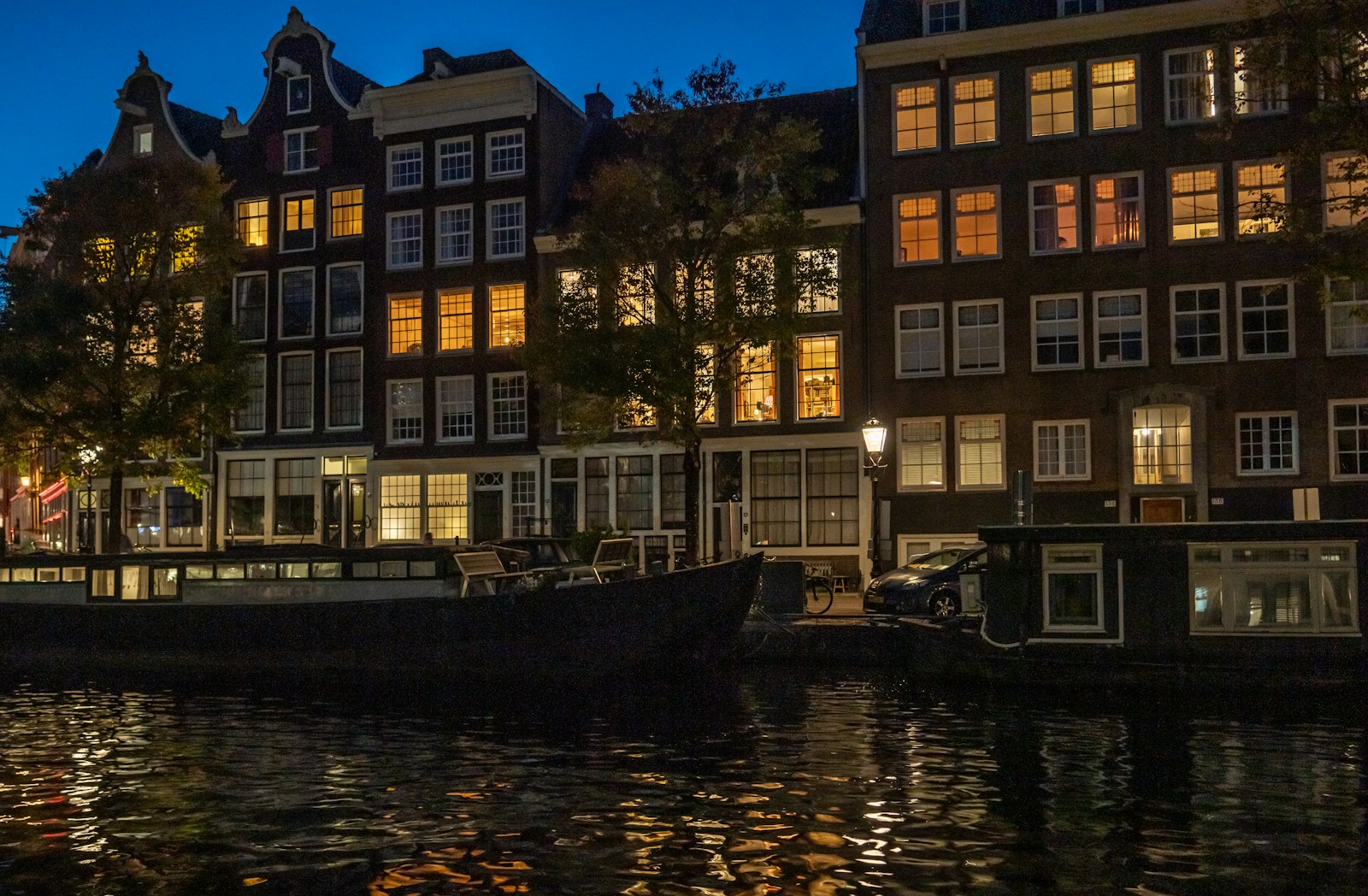 Illuminated narrow canal houses and a houseboat reflected on Amsterdam water at night