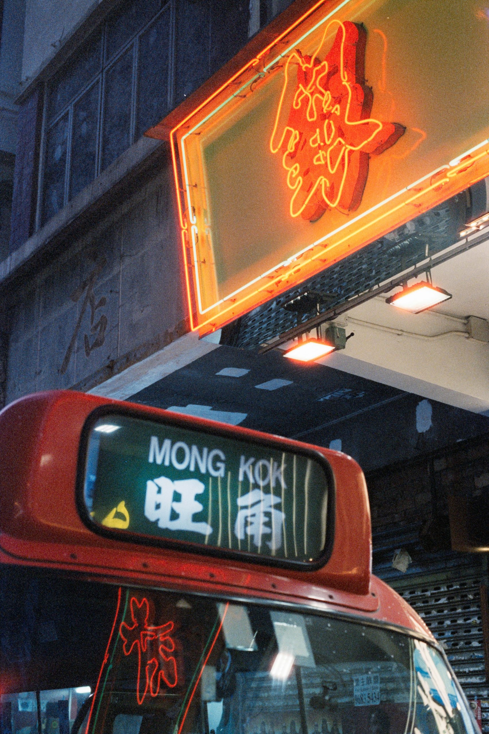 Red minibus with Mong Kok destination sign beneath a neon sign at night in Kowloon, Hong Kong