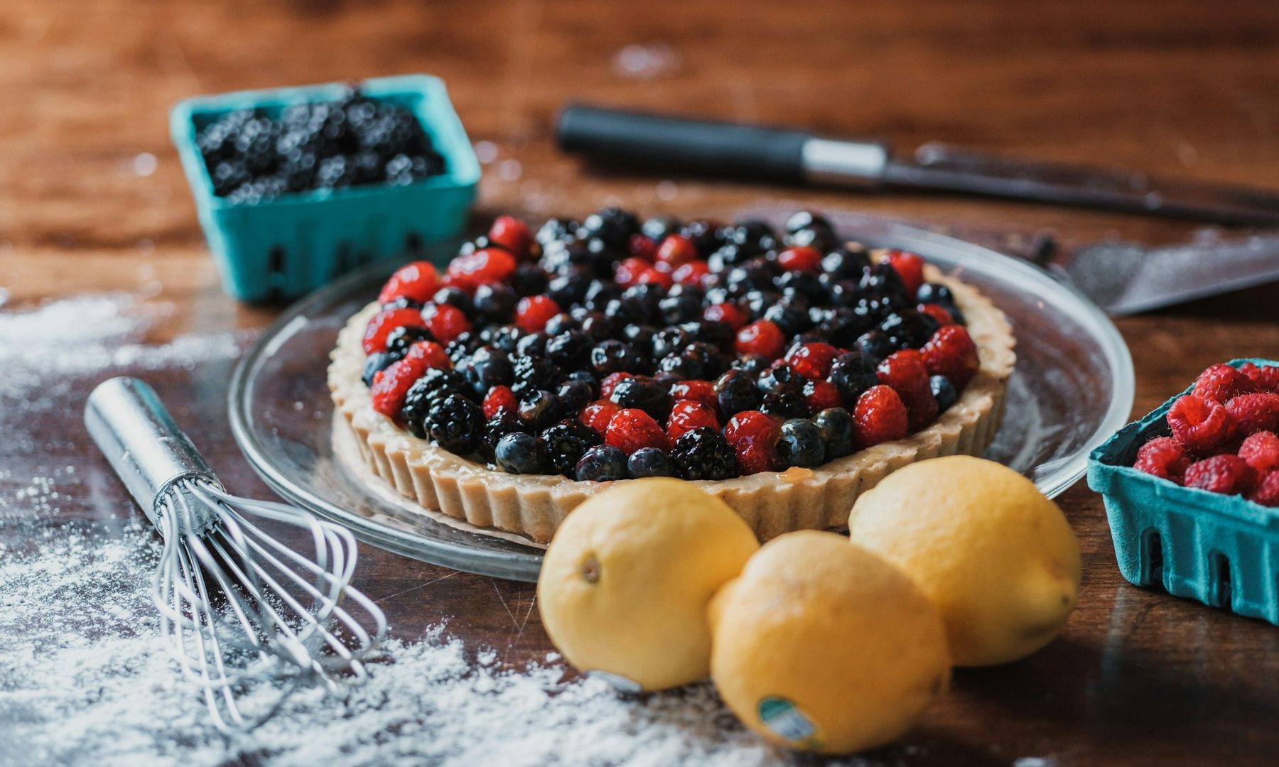 Berry tart with raspberries and blueberries beside lemons on a wooden table