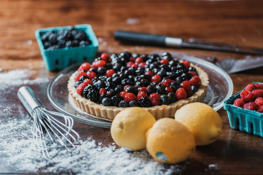 Berry tart with raspberries and blueberries beside lemons on a wooden table