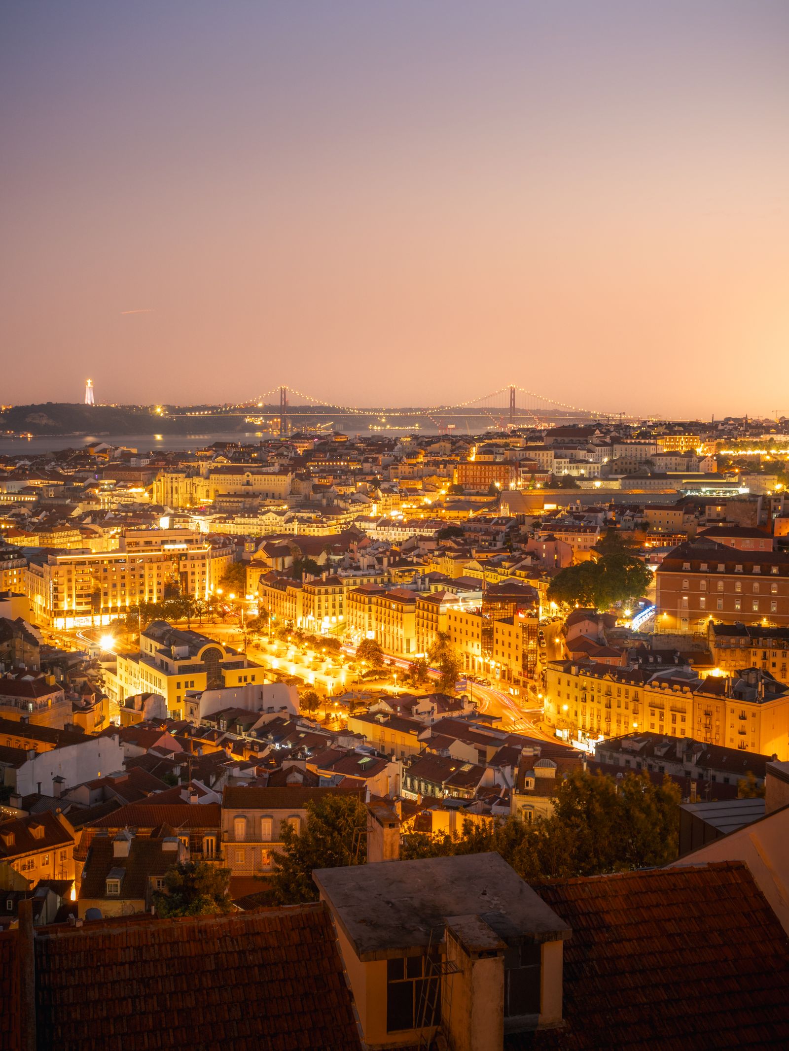Lisbon rooftops and illuminated streets beneath a pink twilight sky