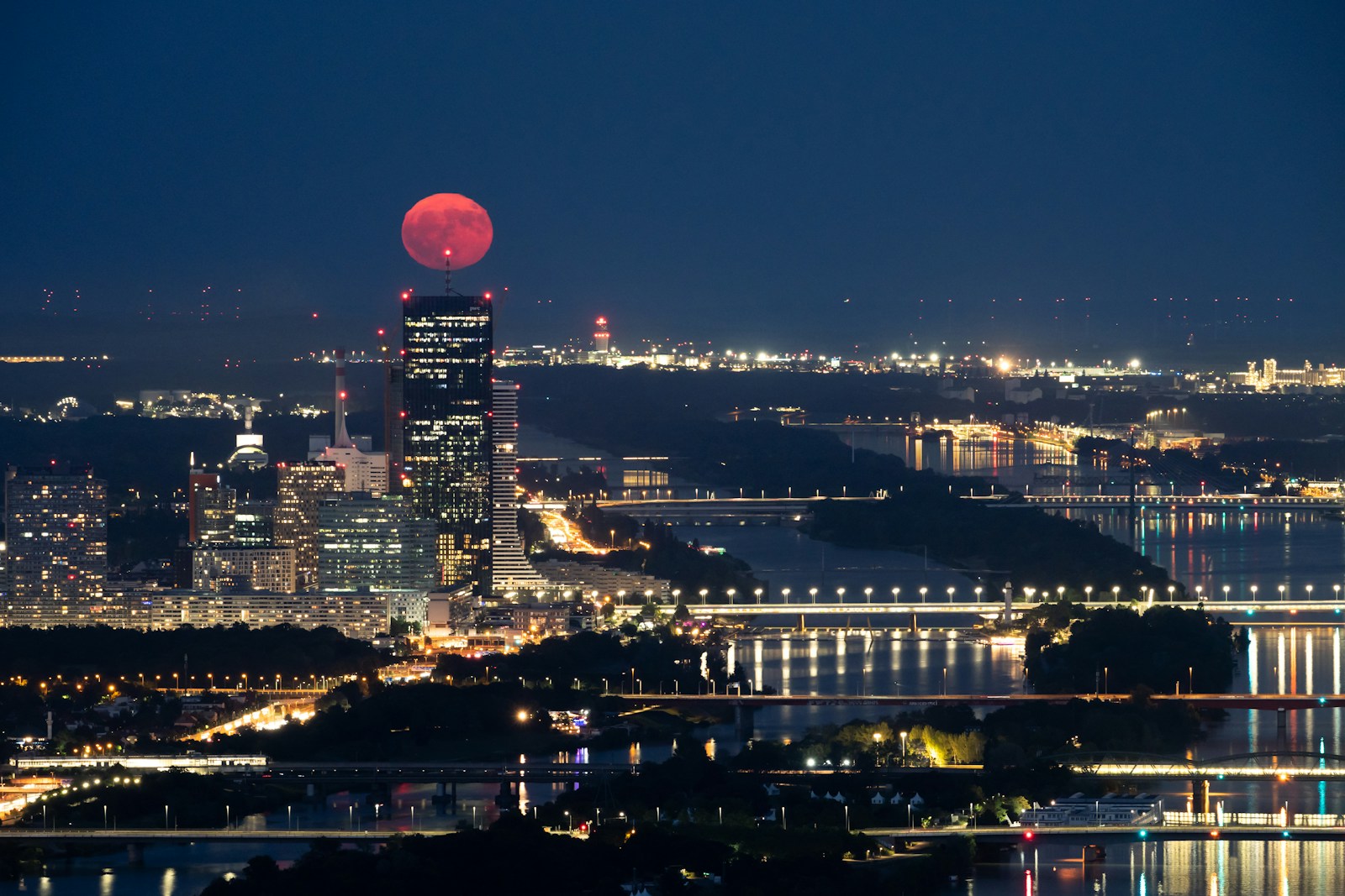 A red moon above Vienna's illuminated skyline and bridges at night