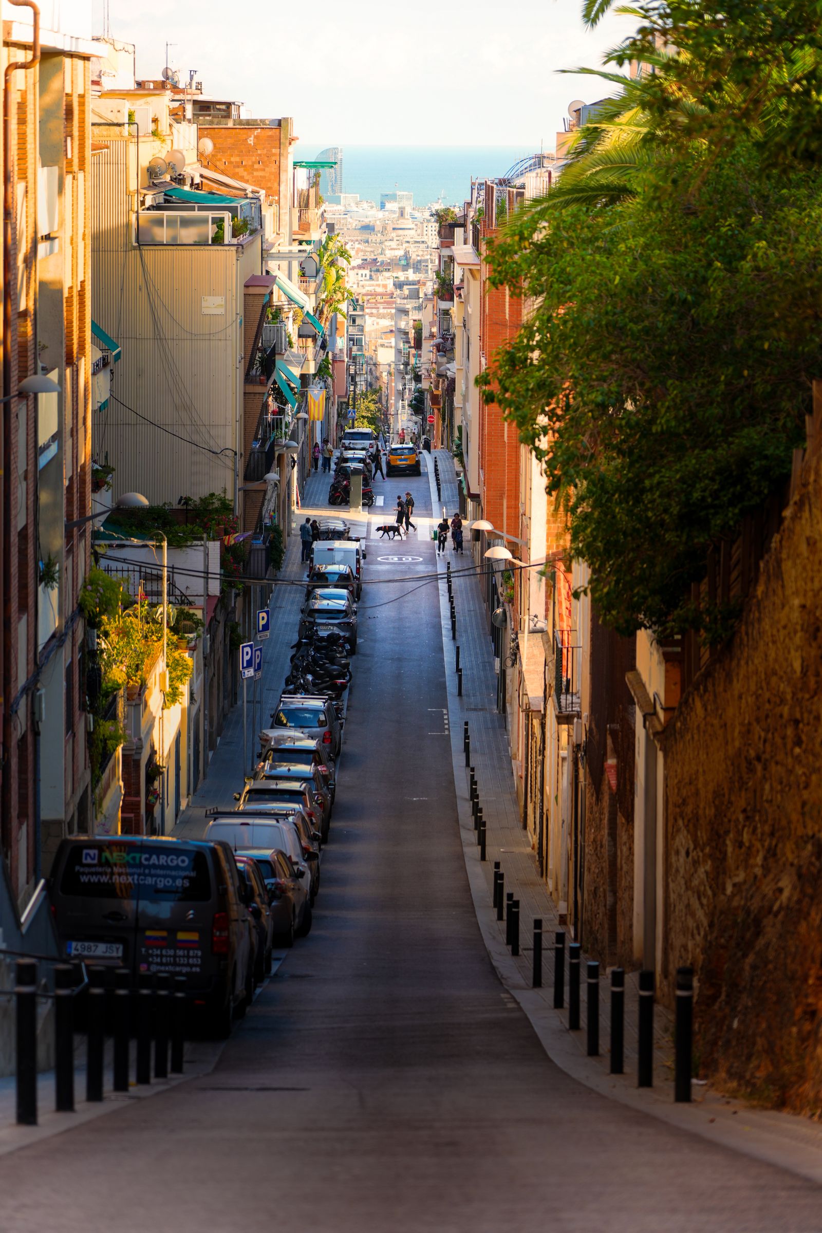 Golden light falls across a descending Barcelona street toward the sea