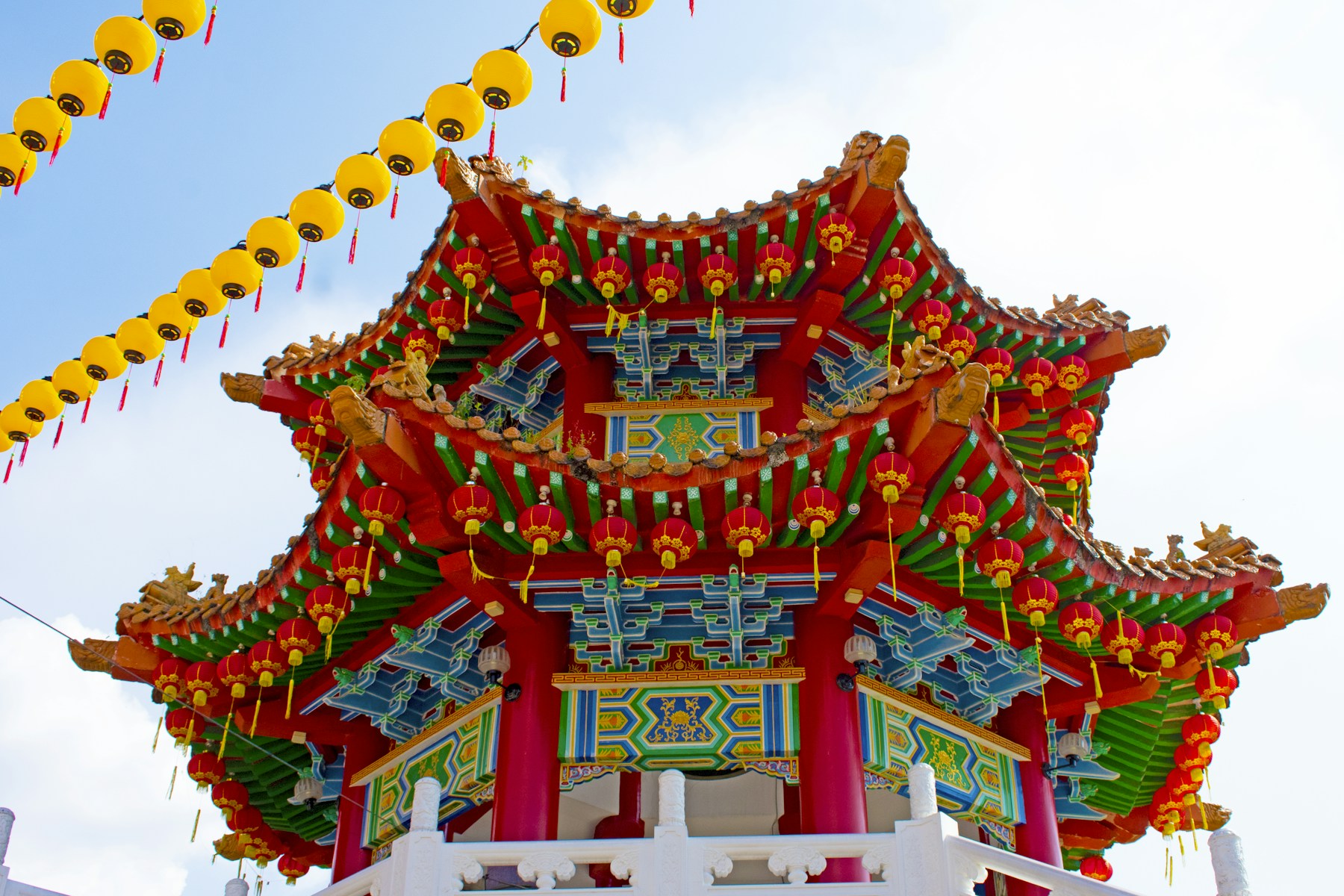 Ornate red and green roof of Thean Hou Temple under rows of yellow lanterns.