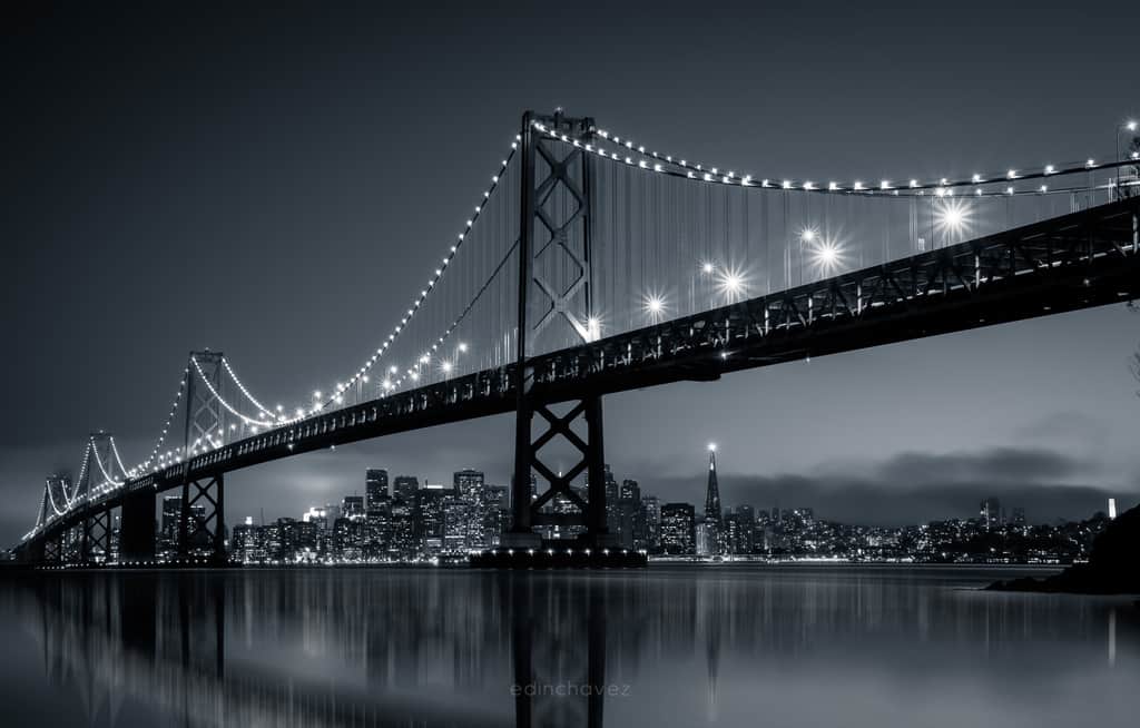 Bay Bridge illuminated over San Francisco skyline and still water at night