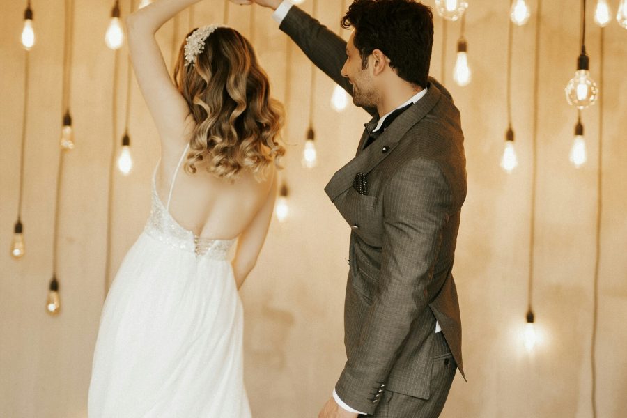 Bride and groom dancing beneath warm hanging bulbs at an indoor wedding reception.