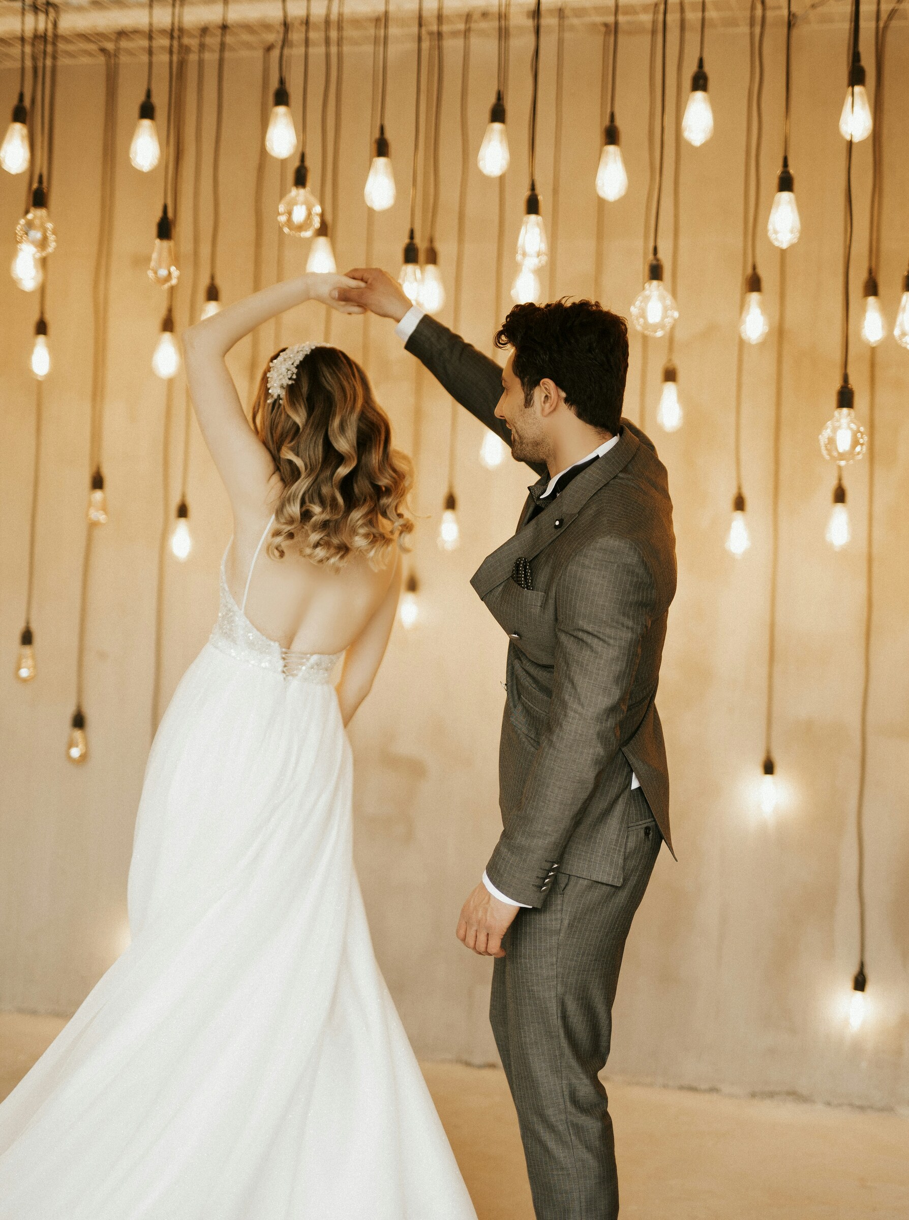Bride and groom dancing beneath warm hanging bulbs at an indoor wedding reception.