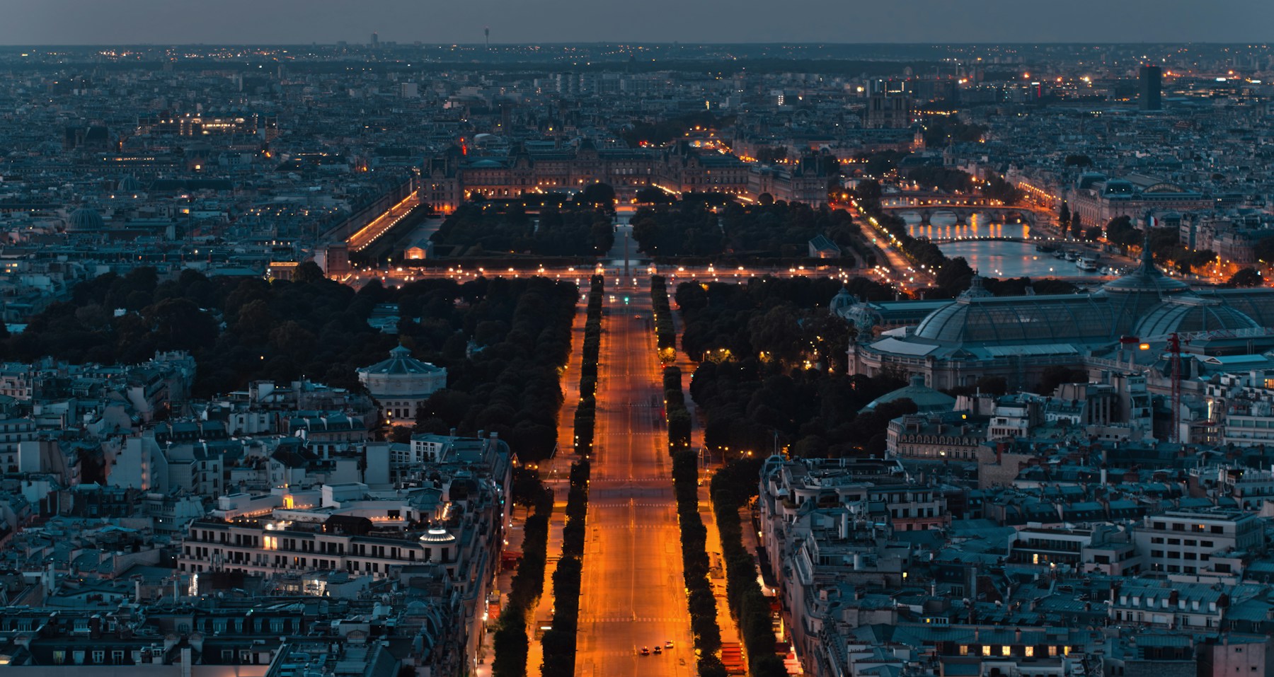 Avenue des Champs-Élysées and the Louvre lit at blue hour from above Paris
