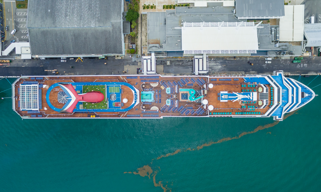 Straight-down aerial view of a colorful cruise ship alongside a port terminal.