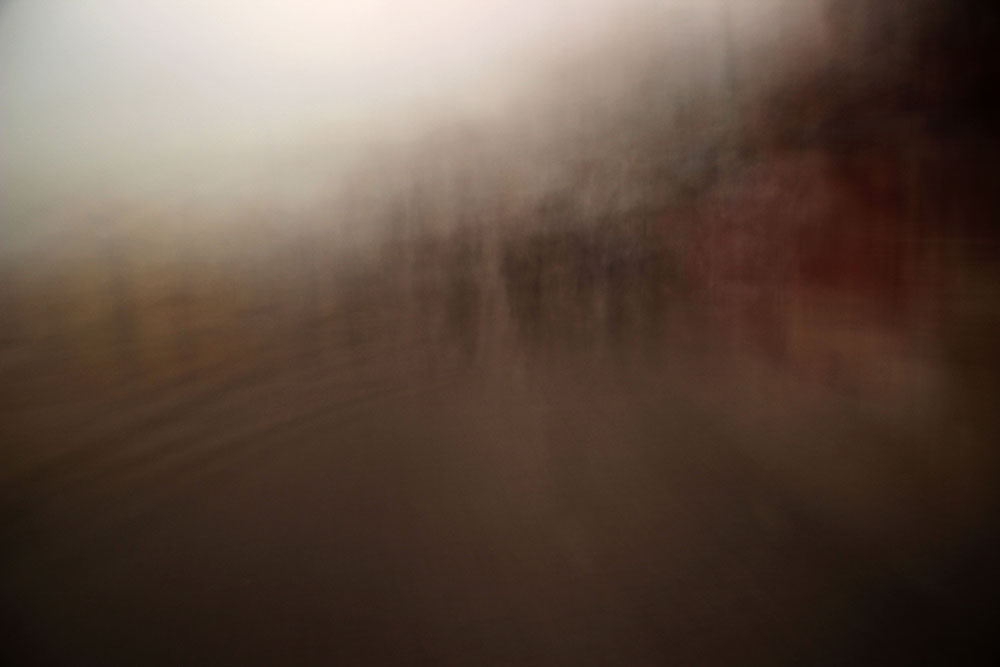 Blurred reflections of trees in brown water beneath a misty sky.