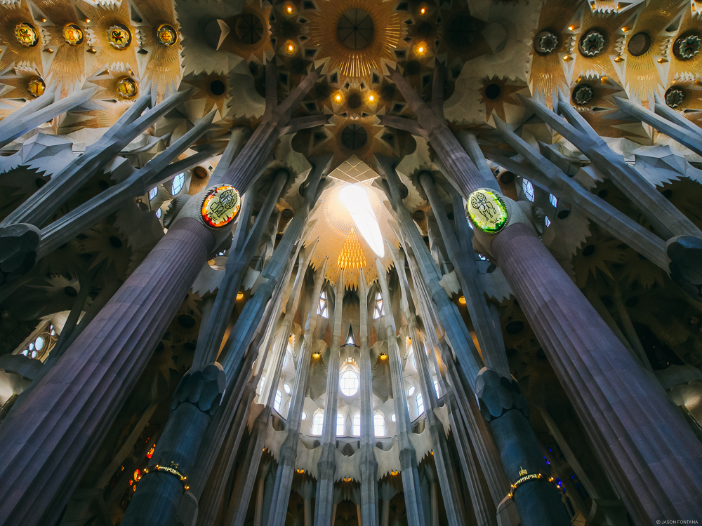 Upward view of tall branching columns and a colorful detailed ceiling inside a large building
