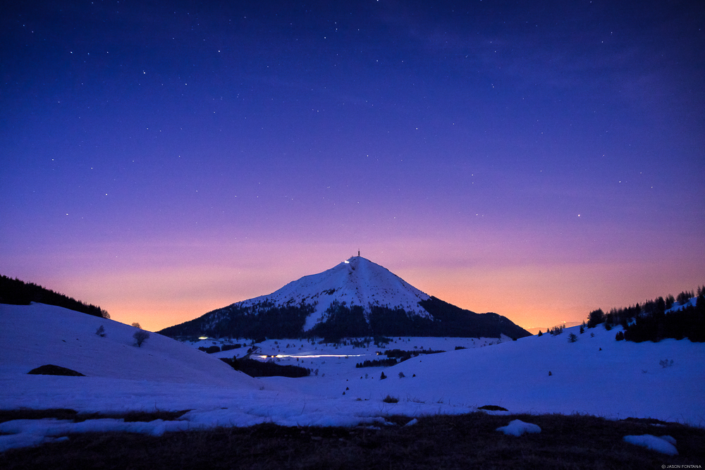 Snow-covered mountain and dark foreground under a purple and orange twilight sky