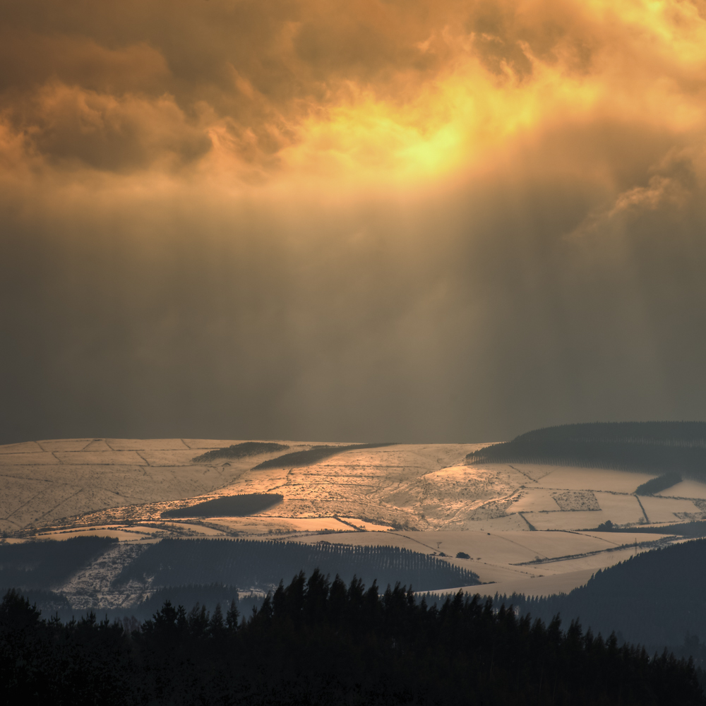 Sun rays breaking through dark clouds over a misty mountain ridge in Galicia
