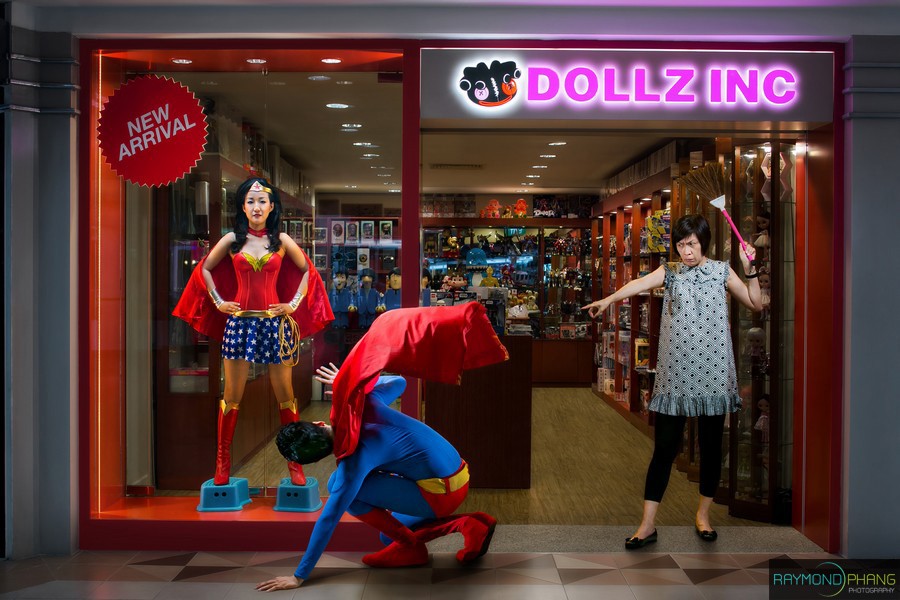 Costumed people pose in front of a toy shop, with one person crouching in a superhero suit.