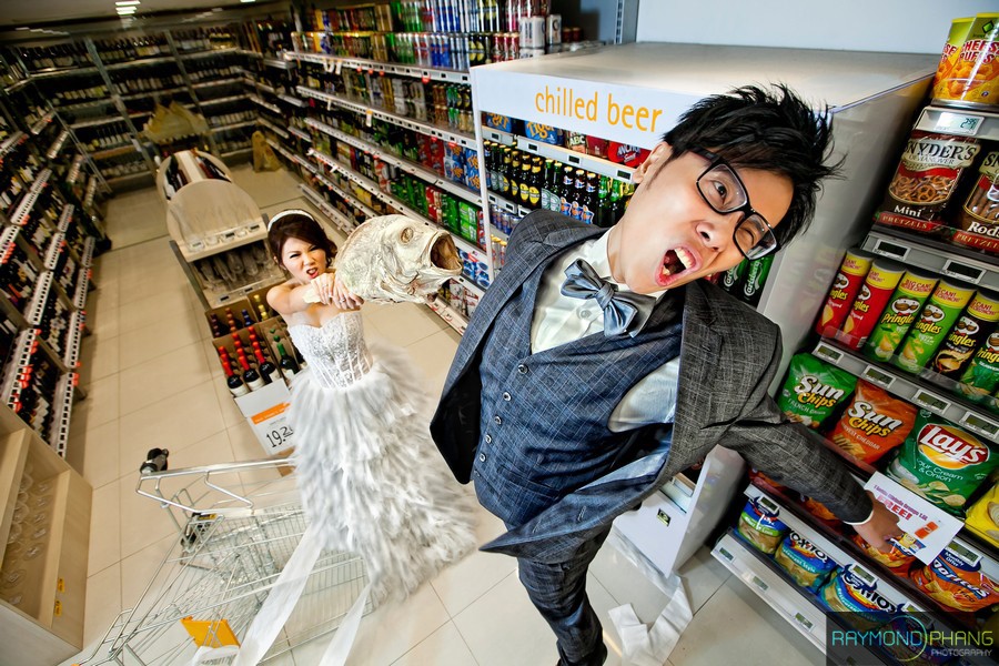 Man poses with an exaggerated expression in a grocery aisle as a woman stands behind him.