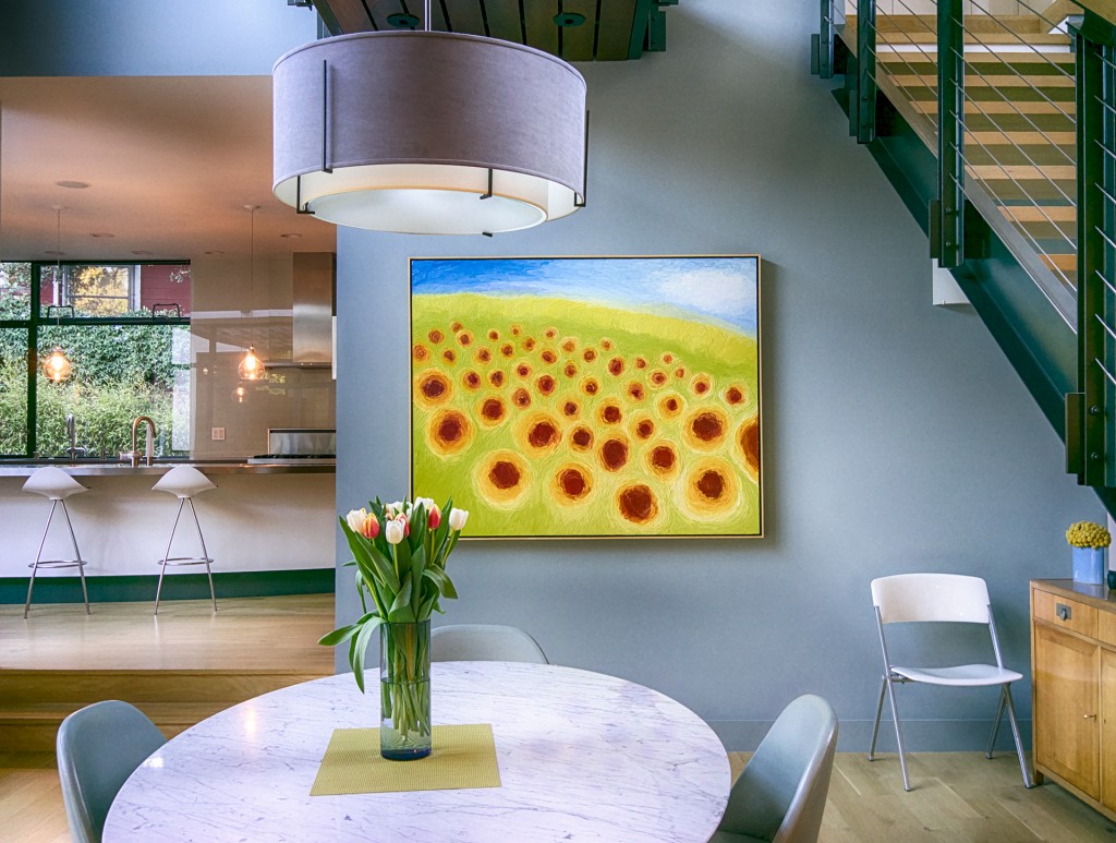 Bright modern room with a dining table, tulips, staircase and sunflower painting.